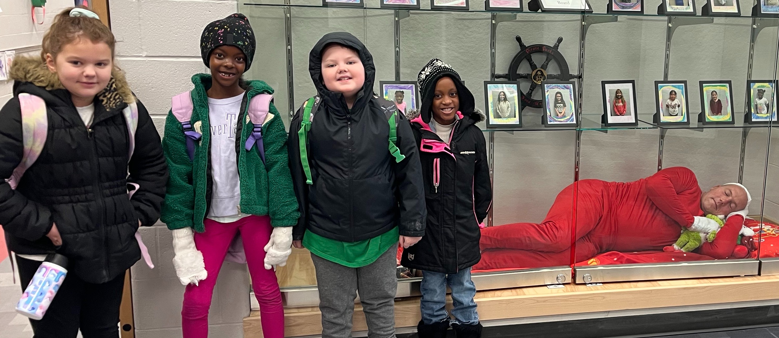 4 children in front of a trophy case with a sleeping elf