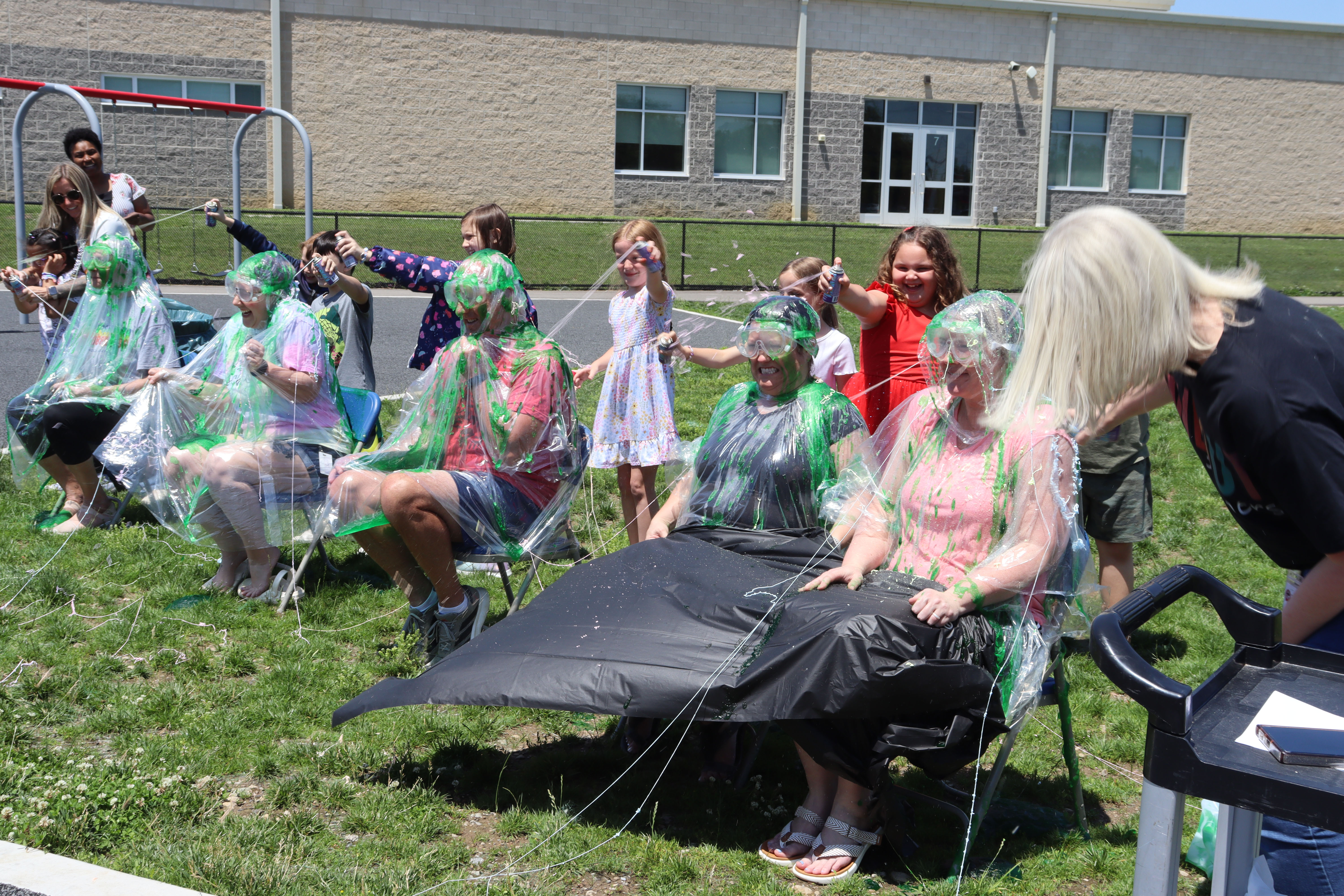 A group of people wearing ponchos are sitting on chairs on a lawn. They are facing forward.