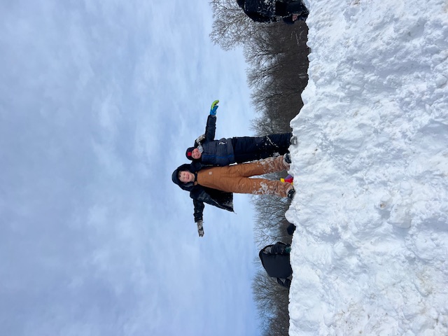 2 students triumphantly standing on top of a snow pile