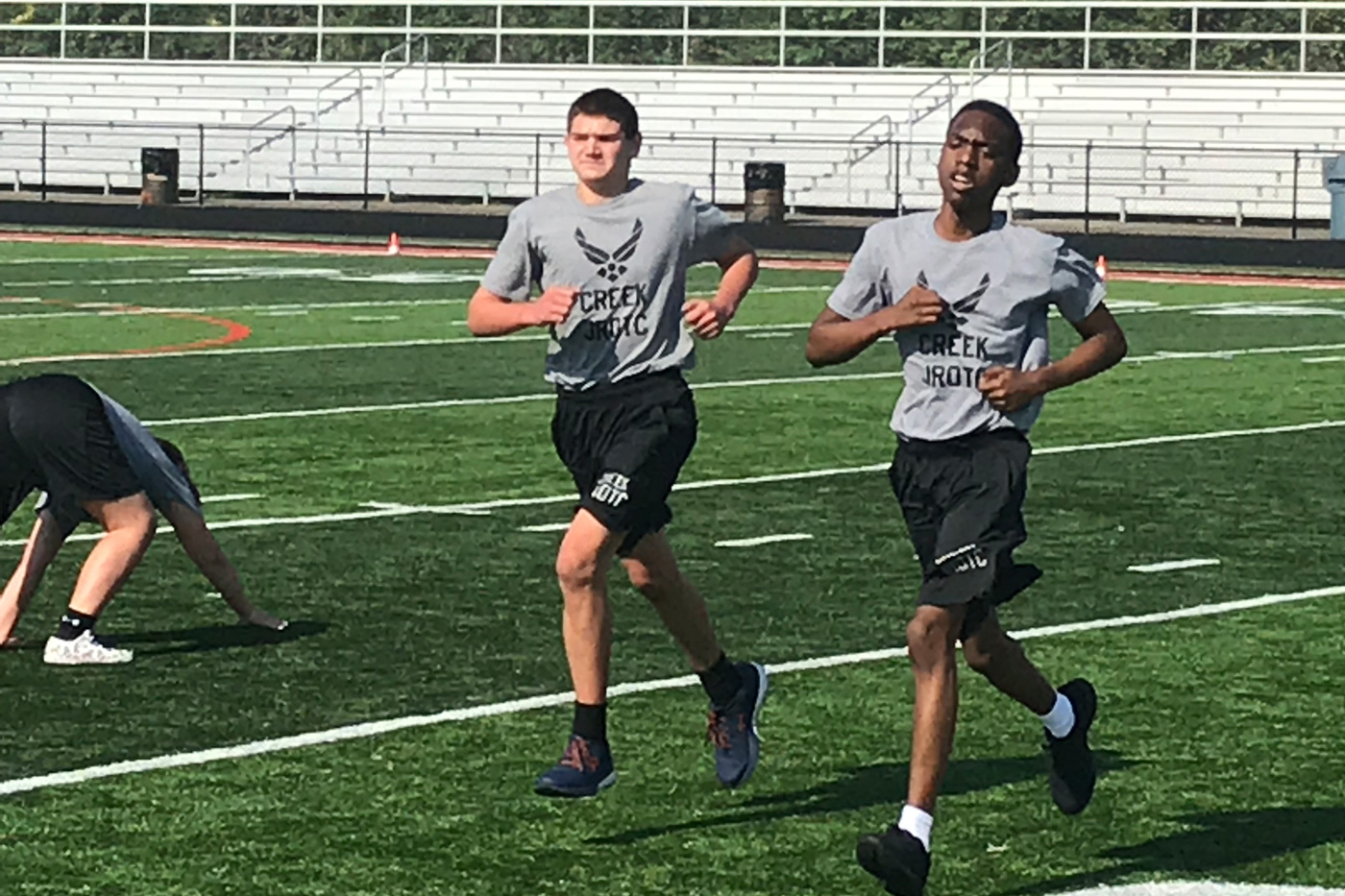 Two young male athletes run on a track field during a practice or race.