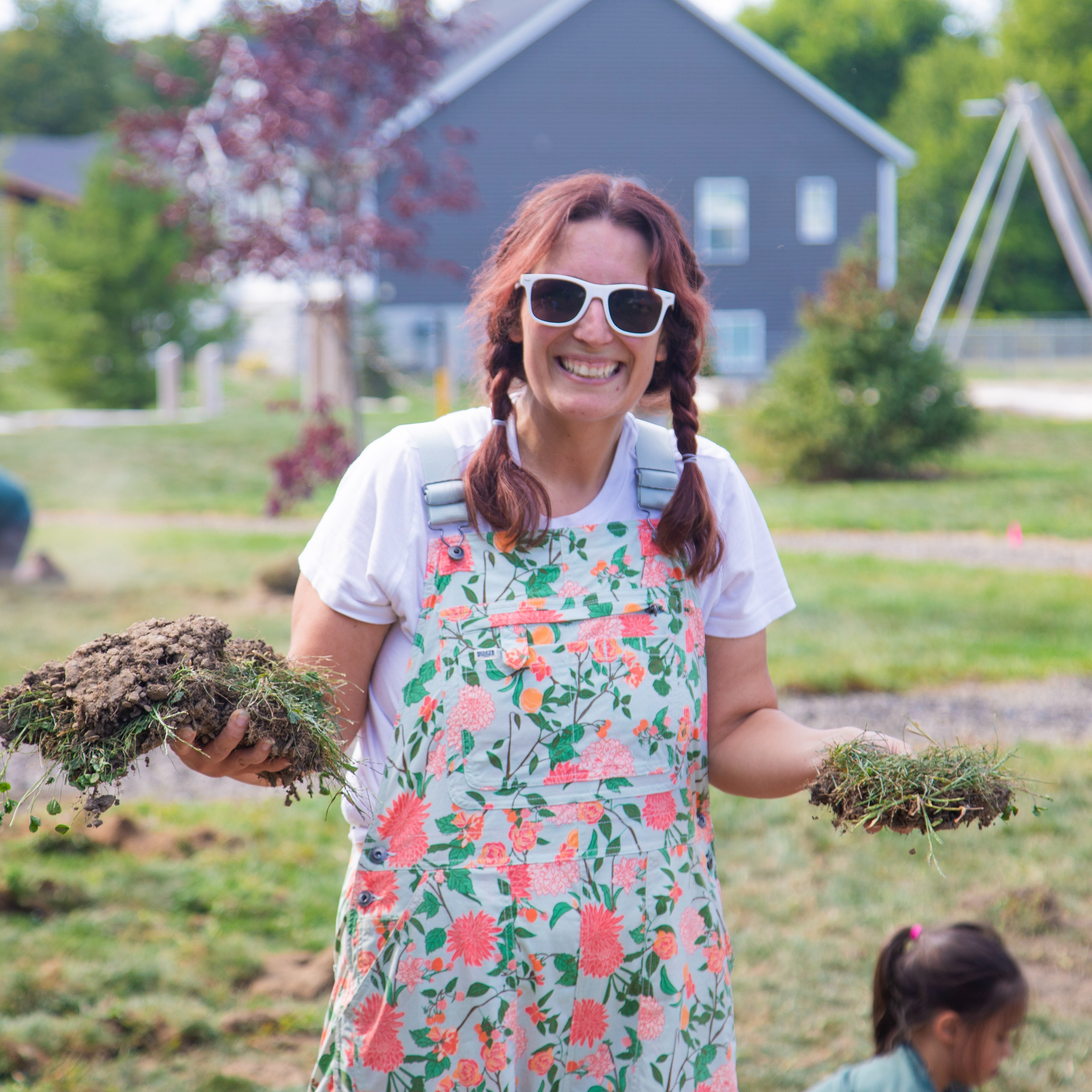 portrait of Ashley Rottman, she is smiling and holding clumps of dirt and grass