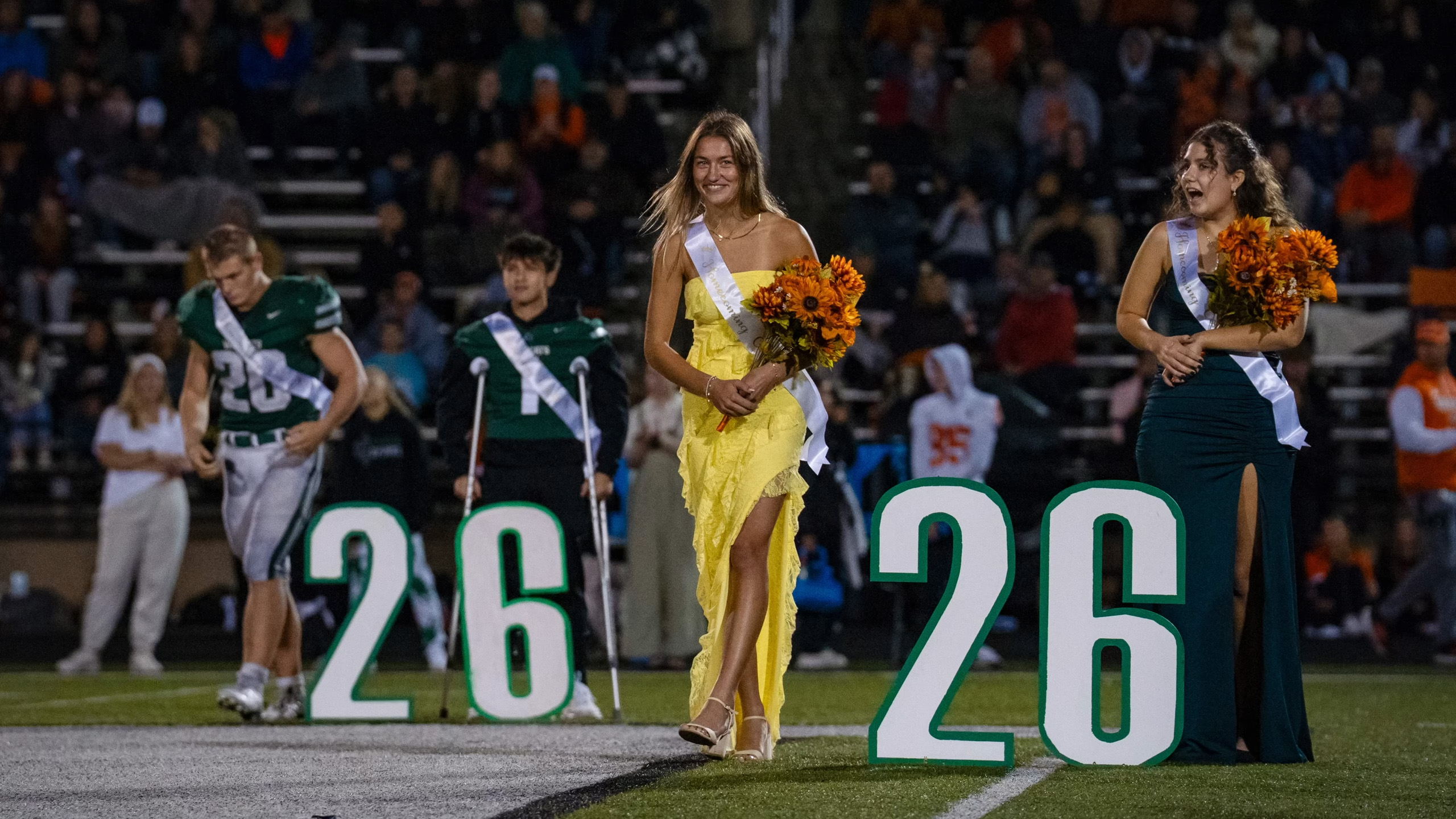 photo from homecoming court with two girls and a football player walking out holding their flowers