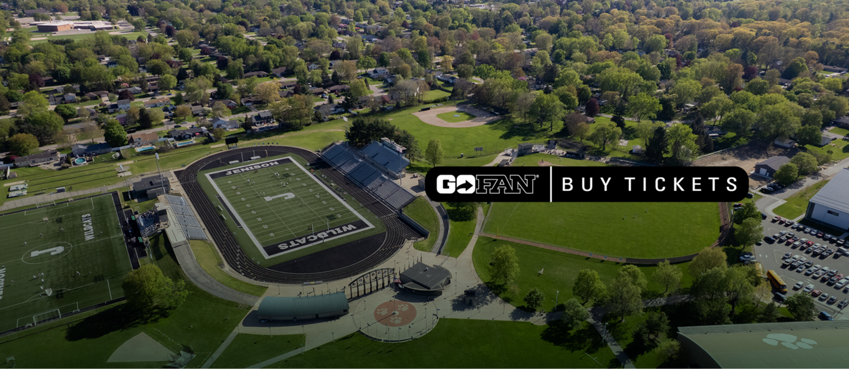 Aerial view of a football field with green grass, stands, and a "Buy Tickets" sign in the foreground.