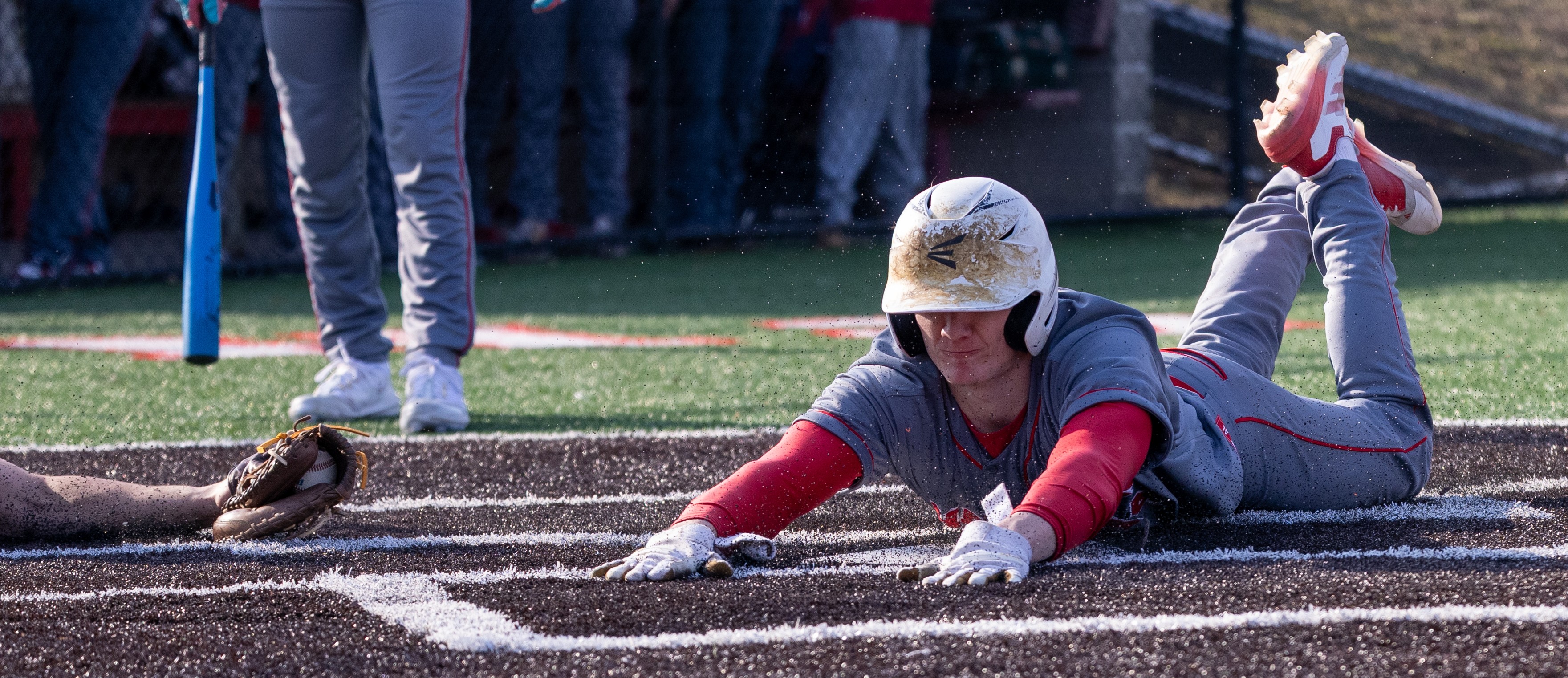 A boy baseball player sliding to home base on their stomach.