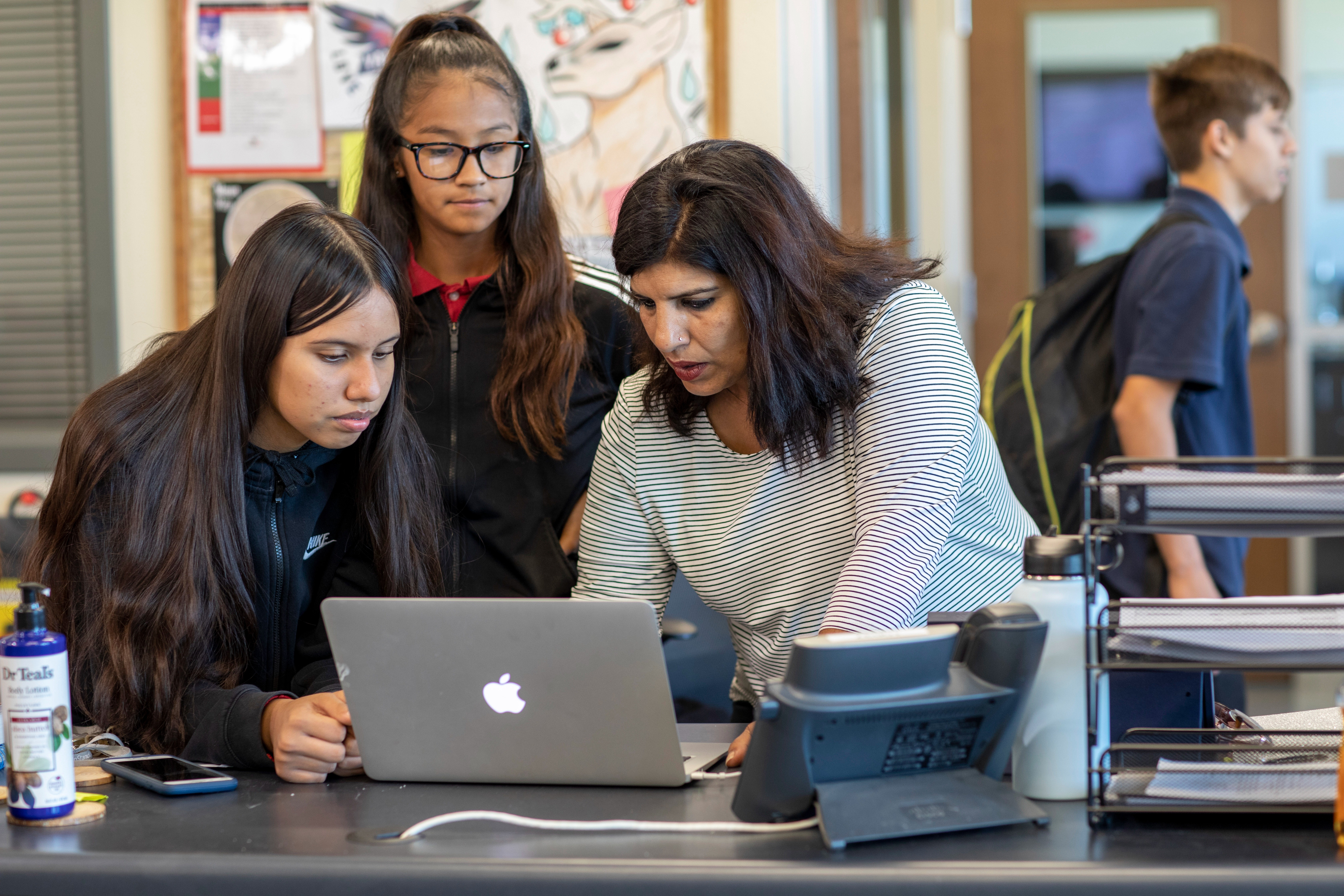 A teacher uses her MacBook to help students with work during class