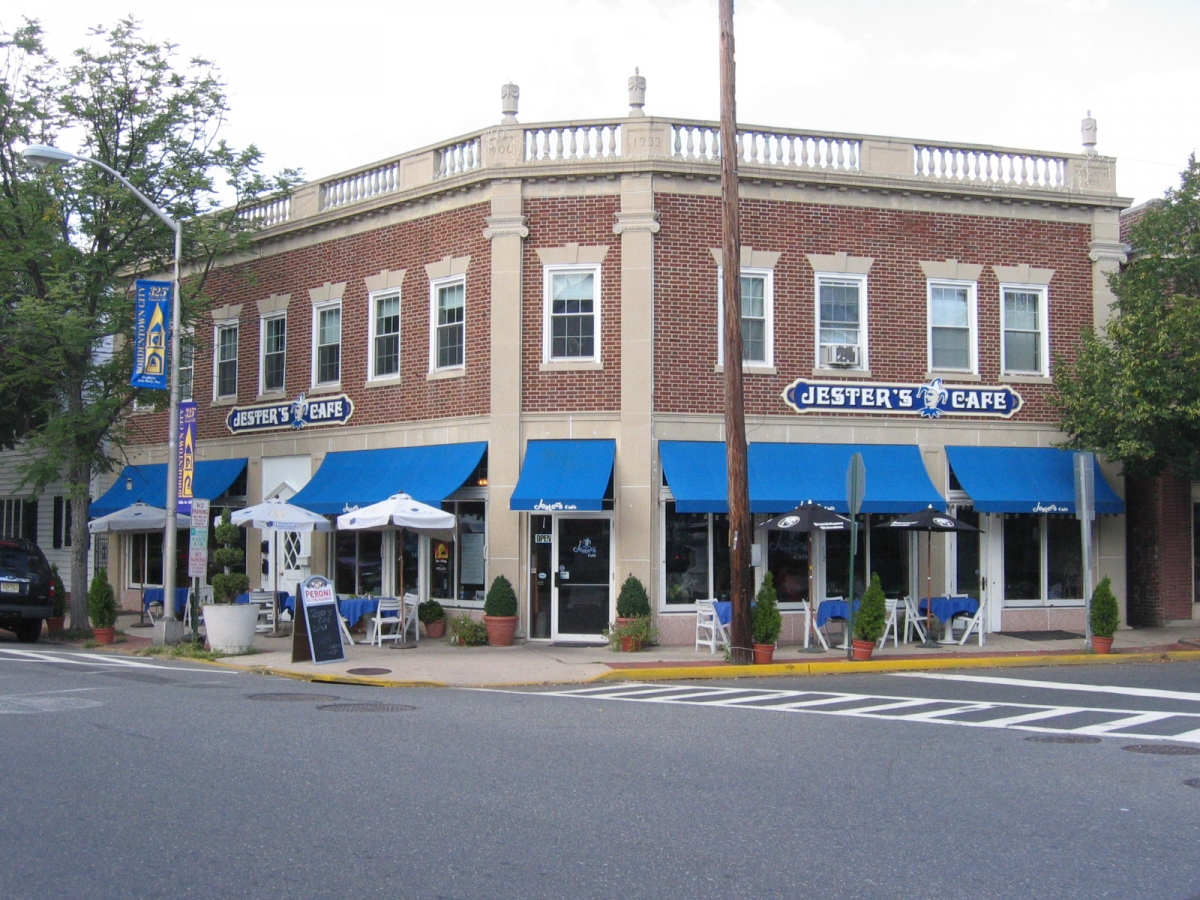 A two-story brick building housing Jester's Cafe with blue awnings and outdoor seating on a street corner.