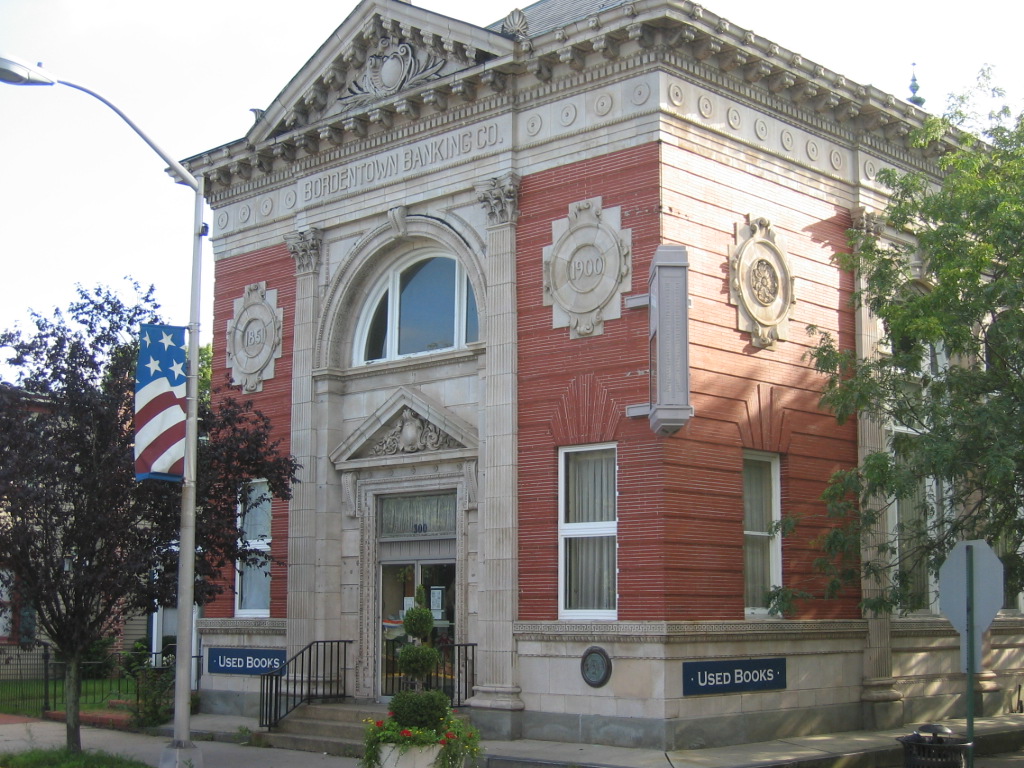 A historic bank building with a red brick facade, white stone accents, and a sign indicating used books outside.
