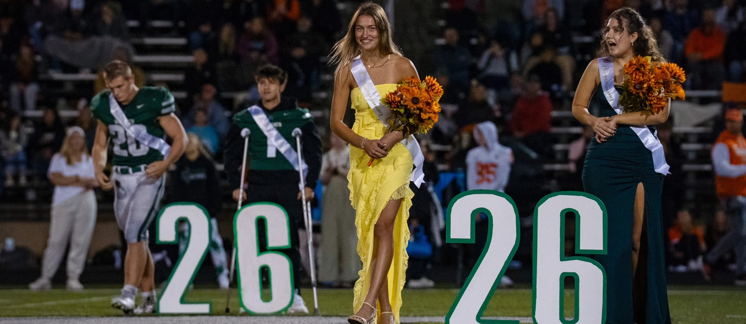 photo from homecoming court with two girls and a football player walking out holding their flowers