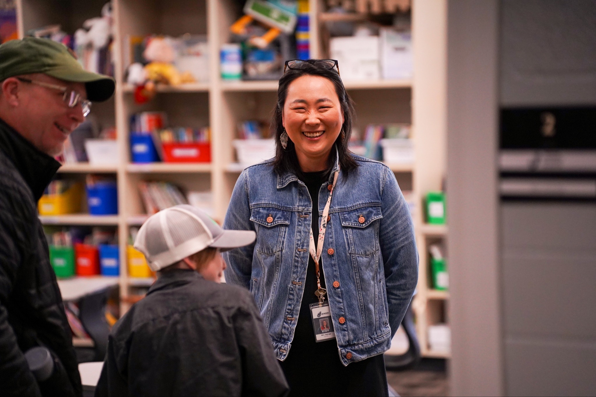 A teacher smiles with a student and parent in the classroom.
