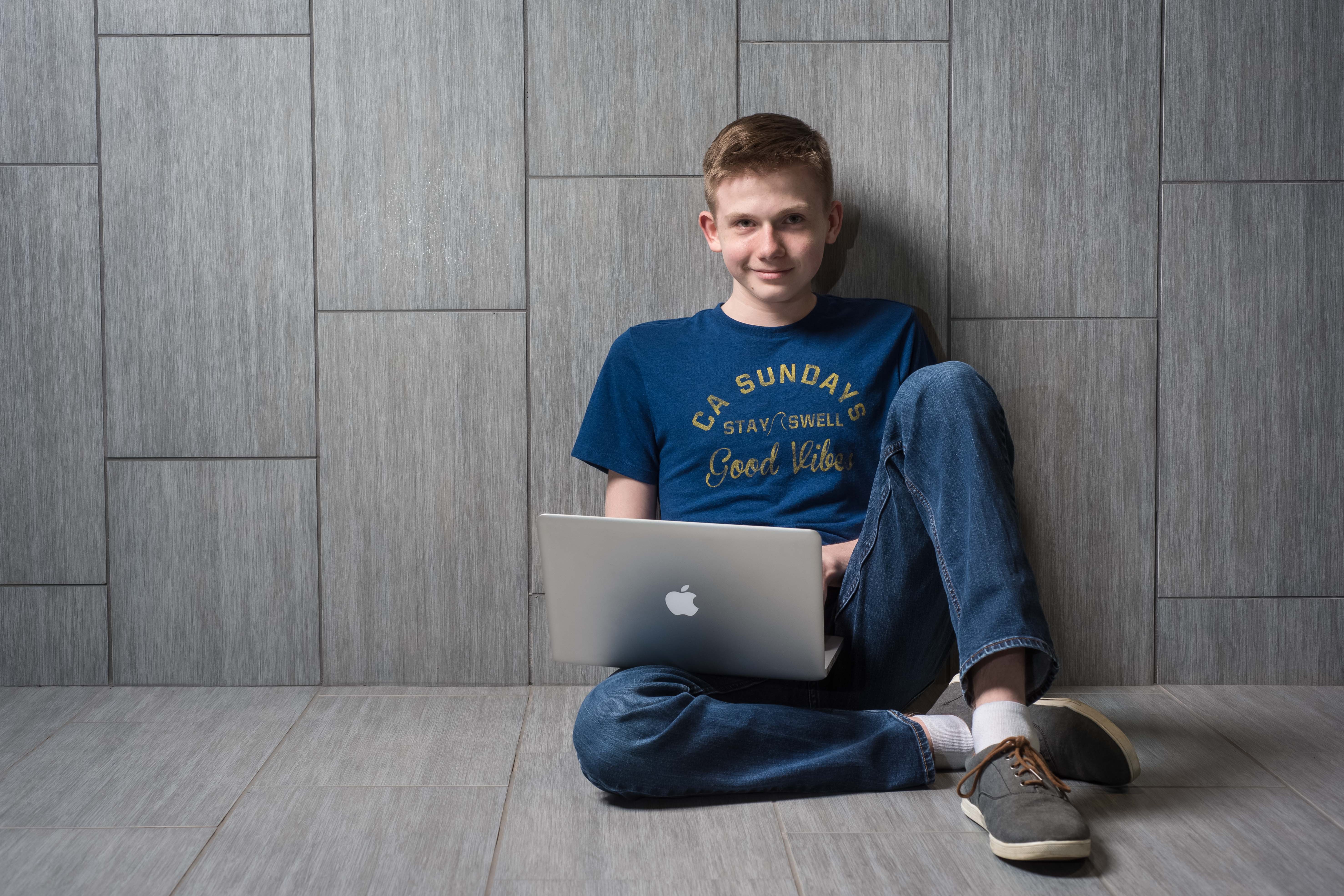 A male student looks into a camera with a laptop.