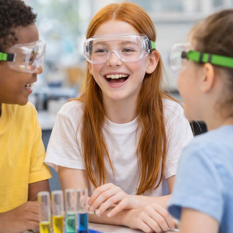 Three children in safety goggles, engaged in a science experiment with beakers of colorful liquid.