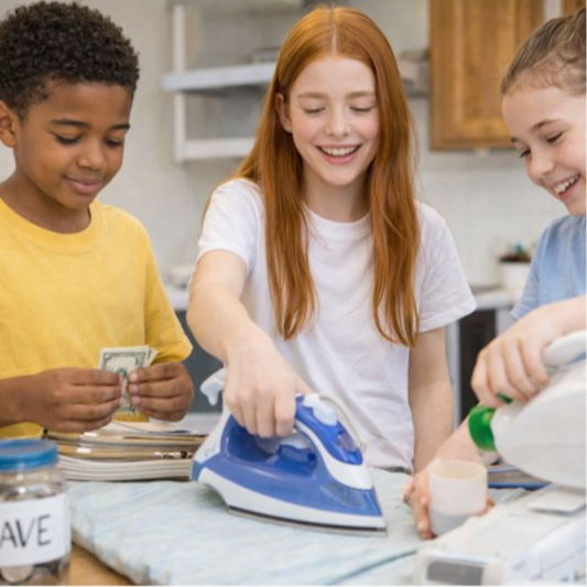 Three children in a kitchen, one holding cash and another ironing a blue cloth.