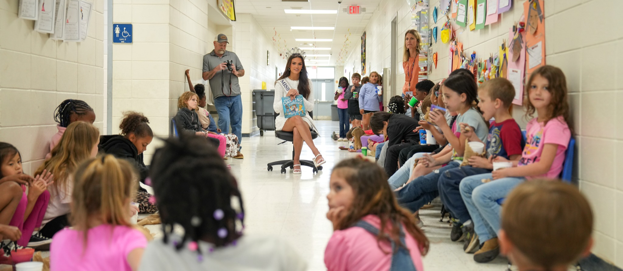 Miss Mississippi Teen is reading to elementary students in a hallway. 