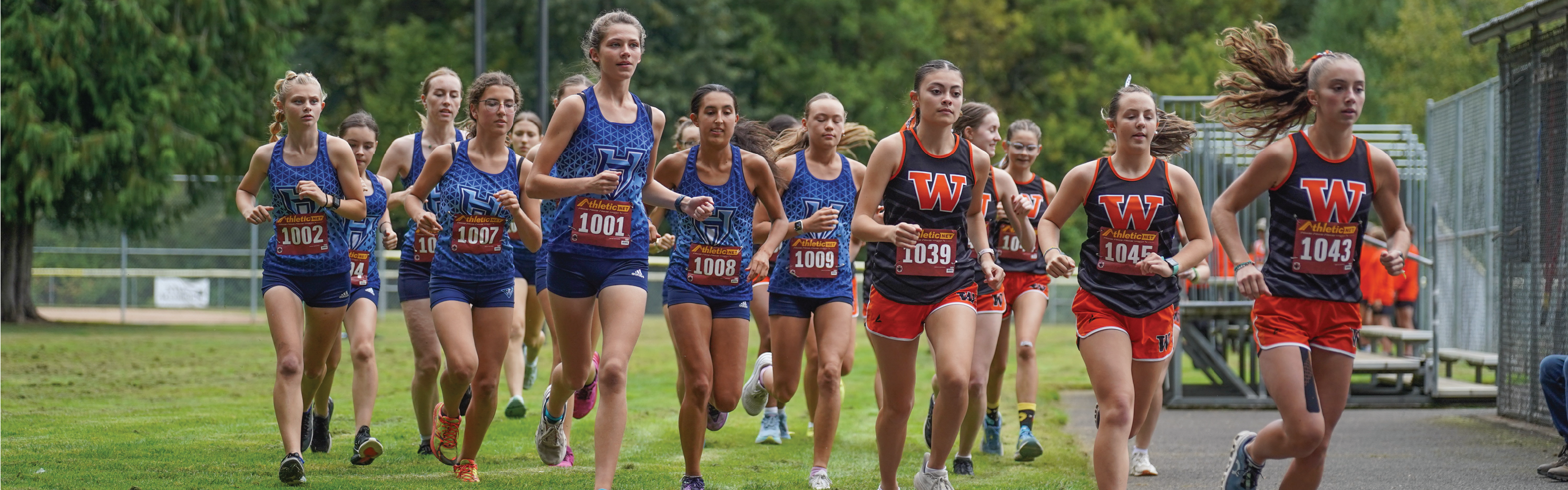 Girls cross country athletes run in a group outdoors.