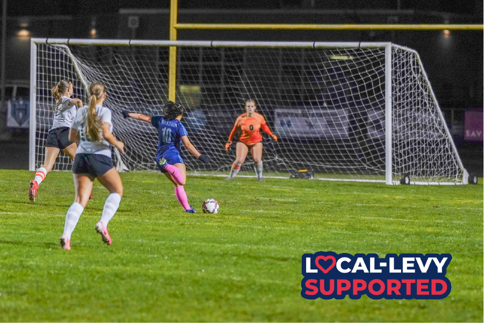 Girls soccer athlete kicks ball toward goal