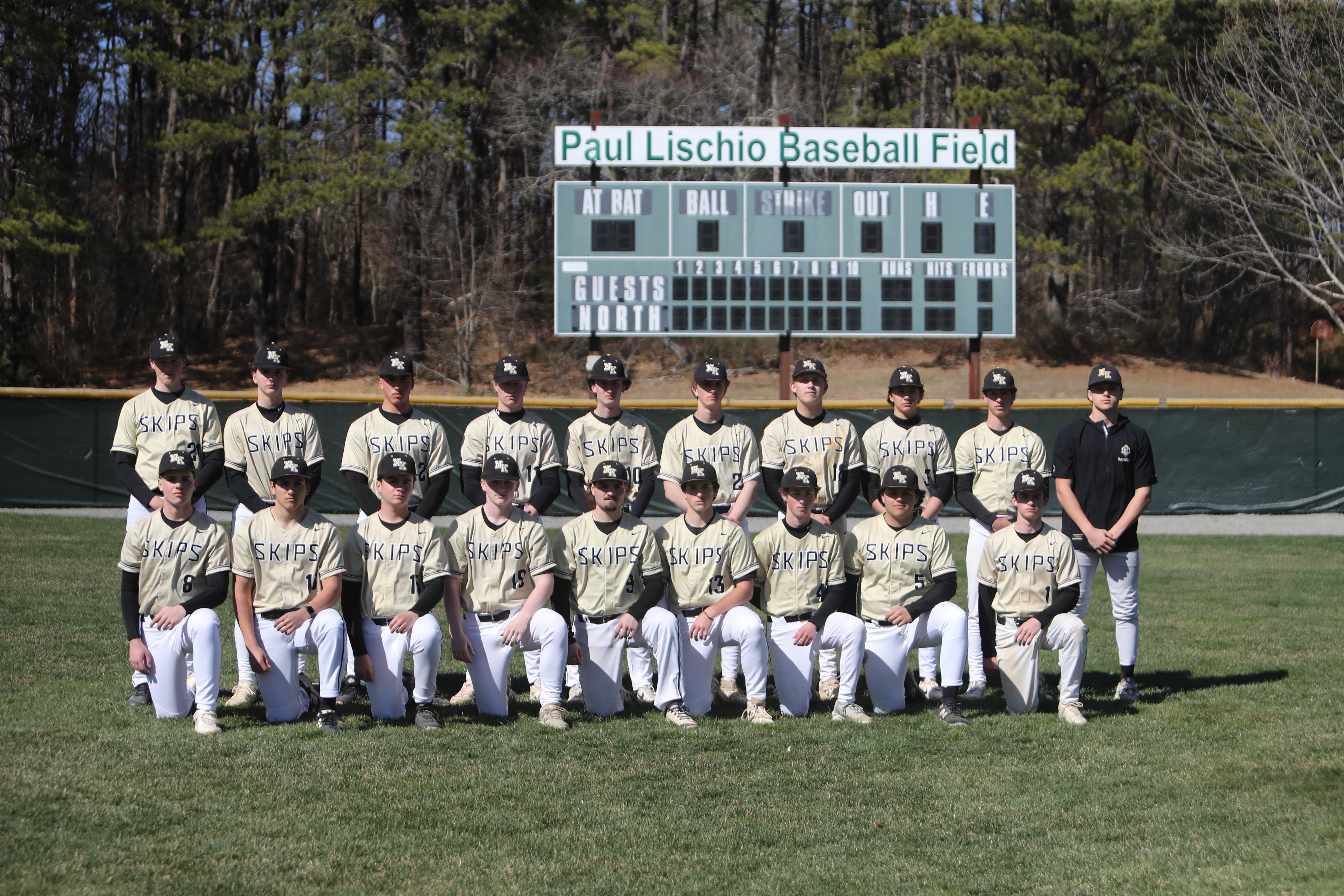 A baseball team in white and black uniforms pose on a field with a large scoreboard.