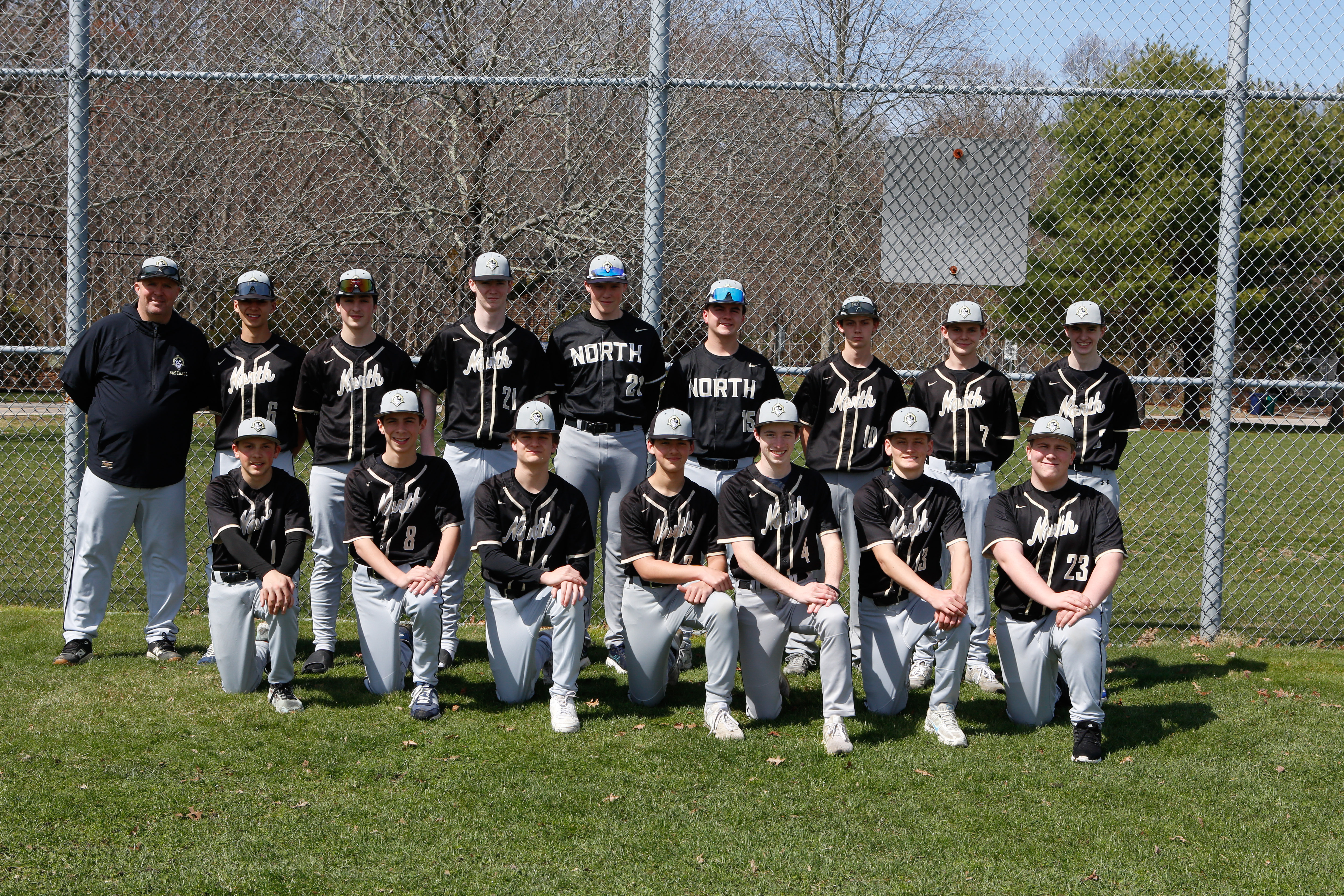 A baseball team stands in two rows on a field with a fence behind them.