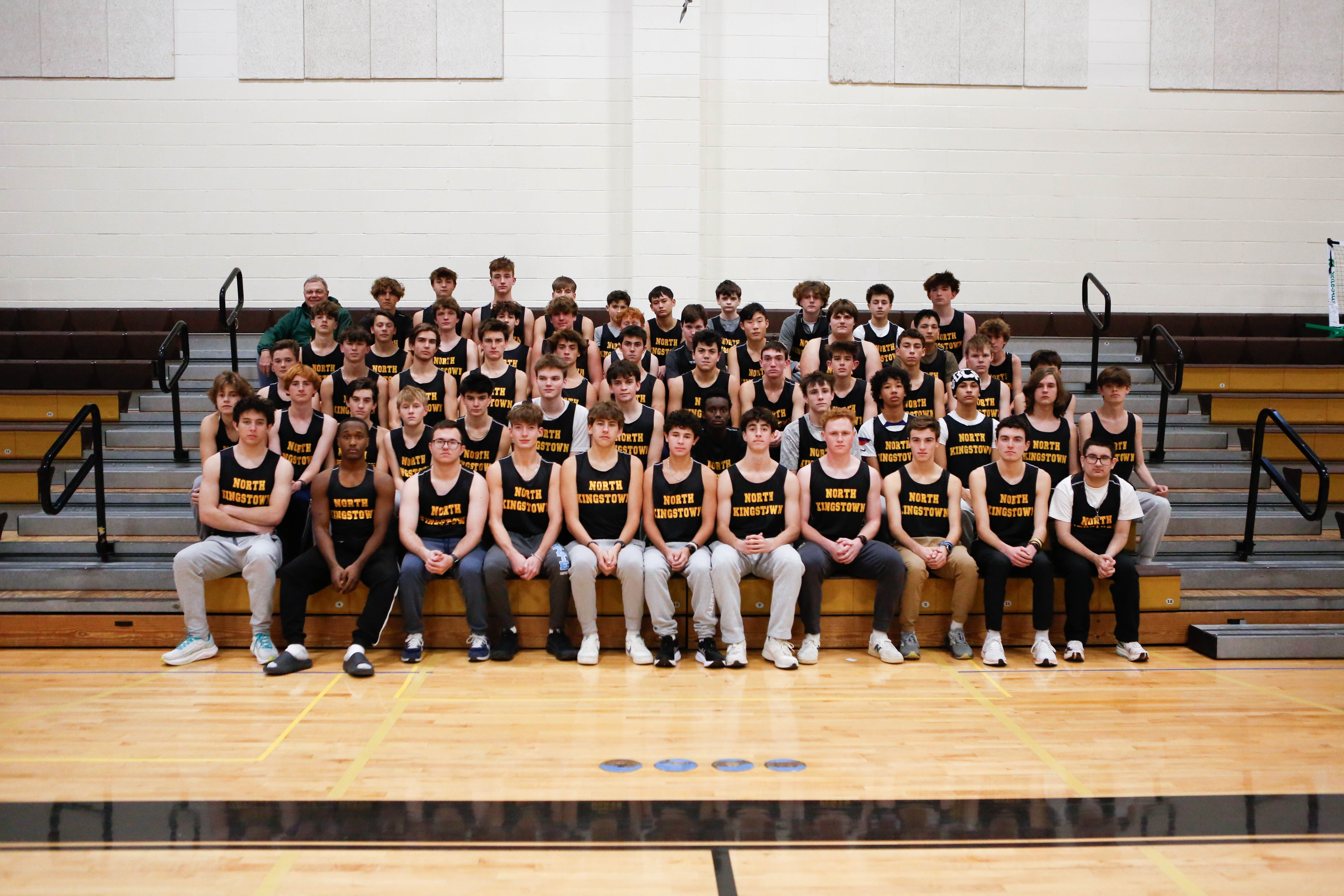 A sports team dressed in black and yellow jerseys, sitting on bleachers inside a gym.