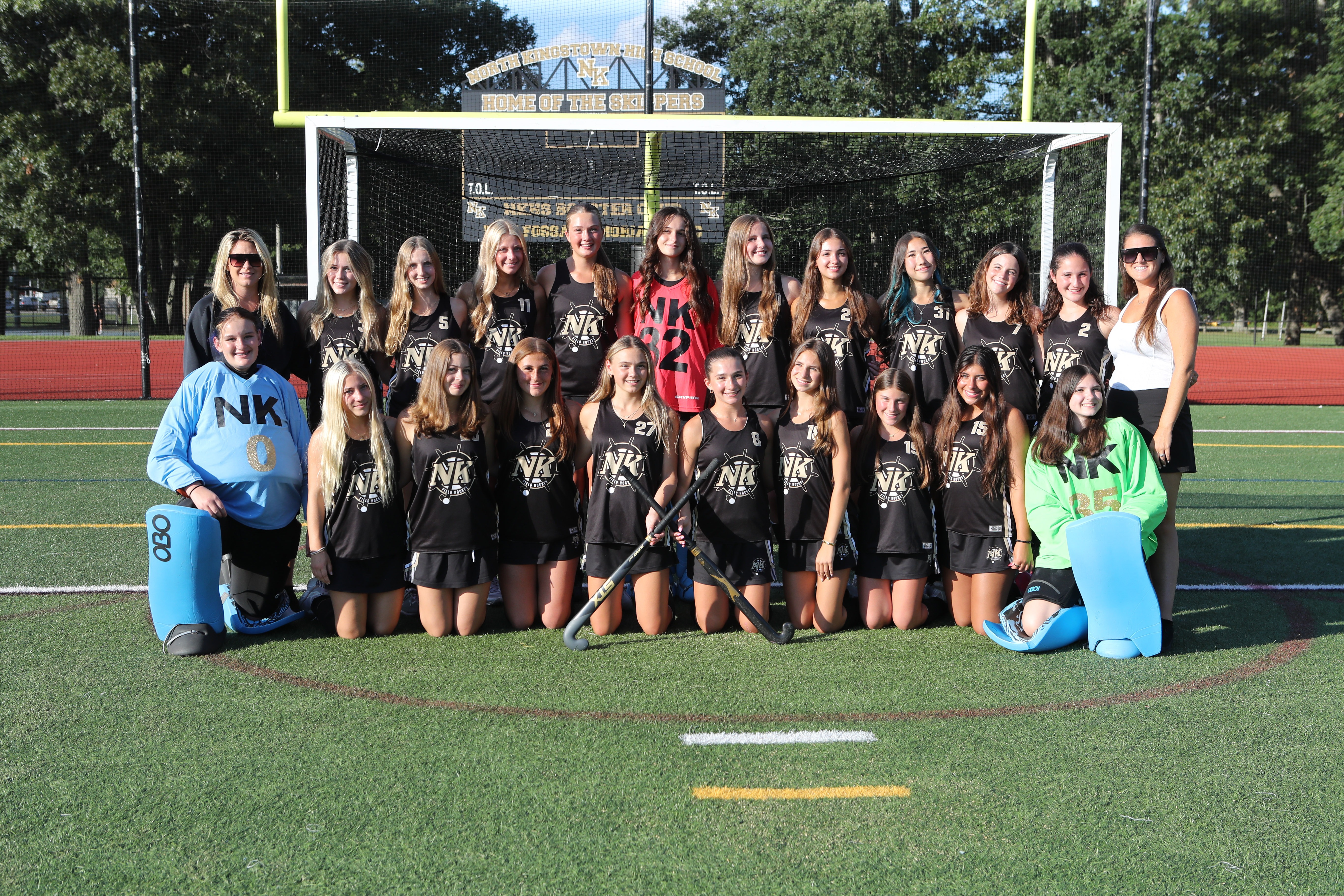 A group of female hockey players in black uniforms pose for a photo on a field.