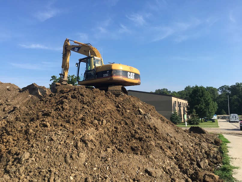 Photo of the mound of dirt next to the high school building is being moved to the back of the elementary school.