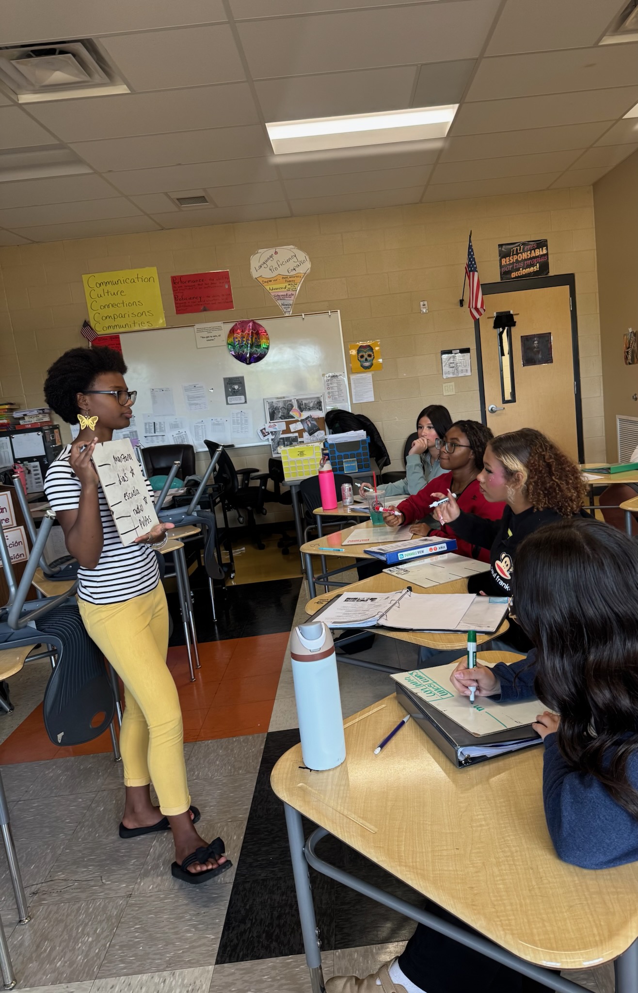National Honor Society student tutoring Spanish I students during Champ Time, standing at front of classroom holding presentation sign while peers take notes at desks