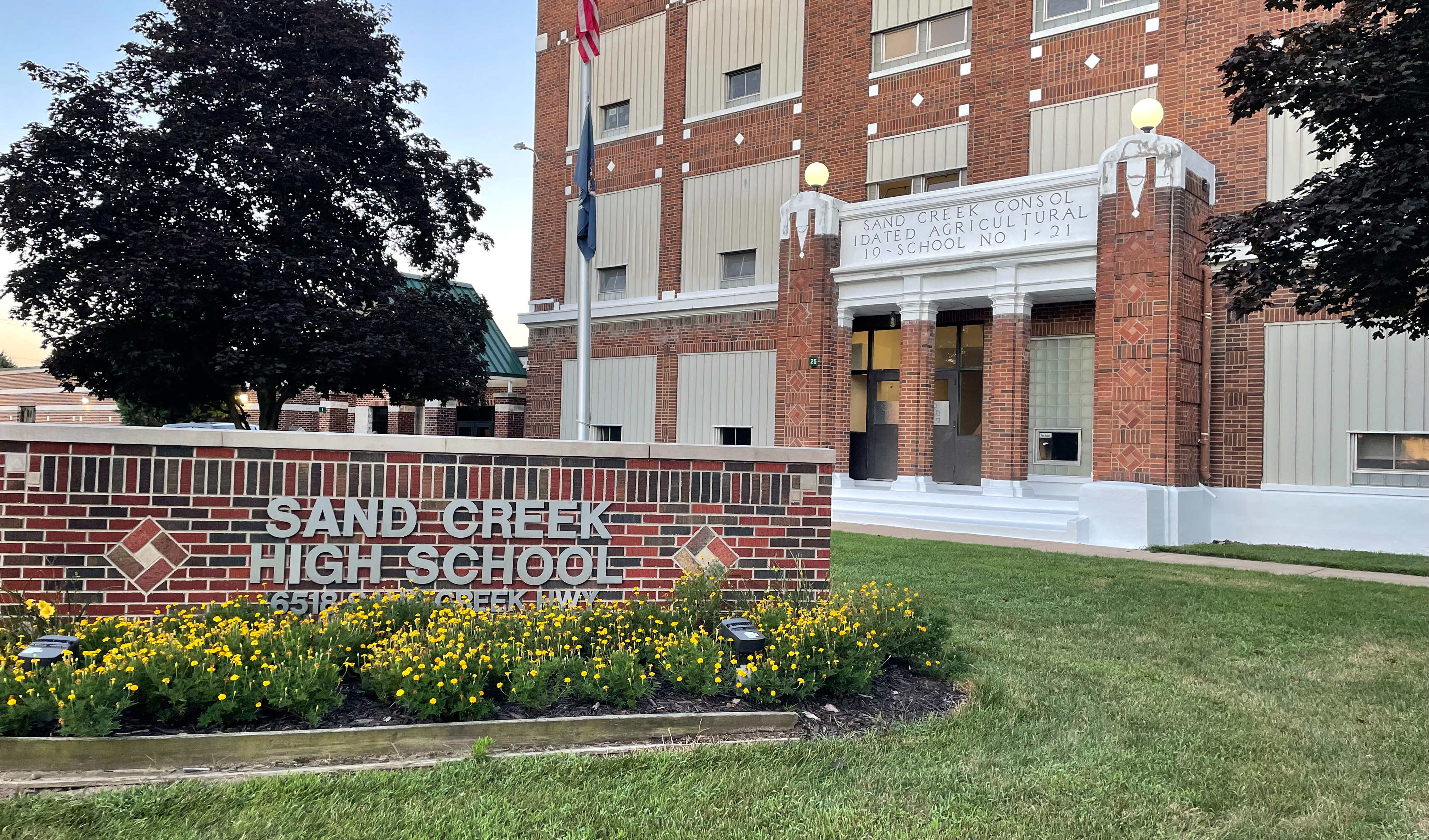 picture of the Sand Creek High School sign on the front lawn with the entrance in the background