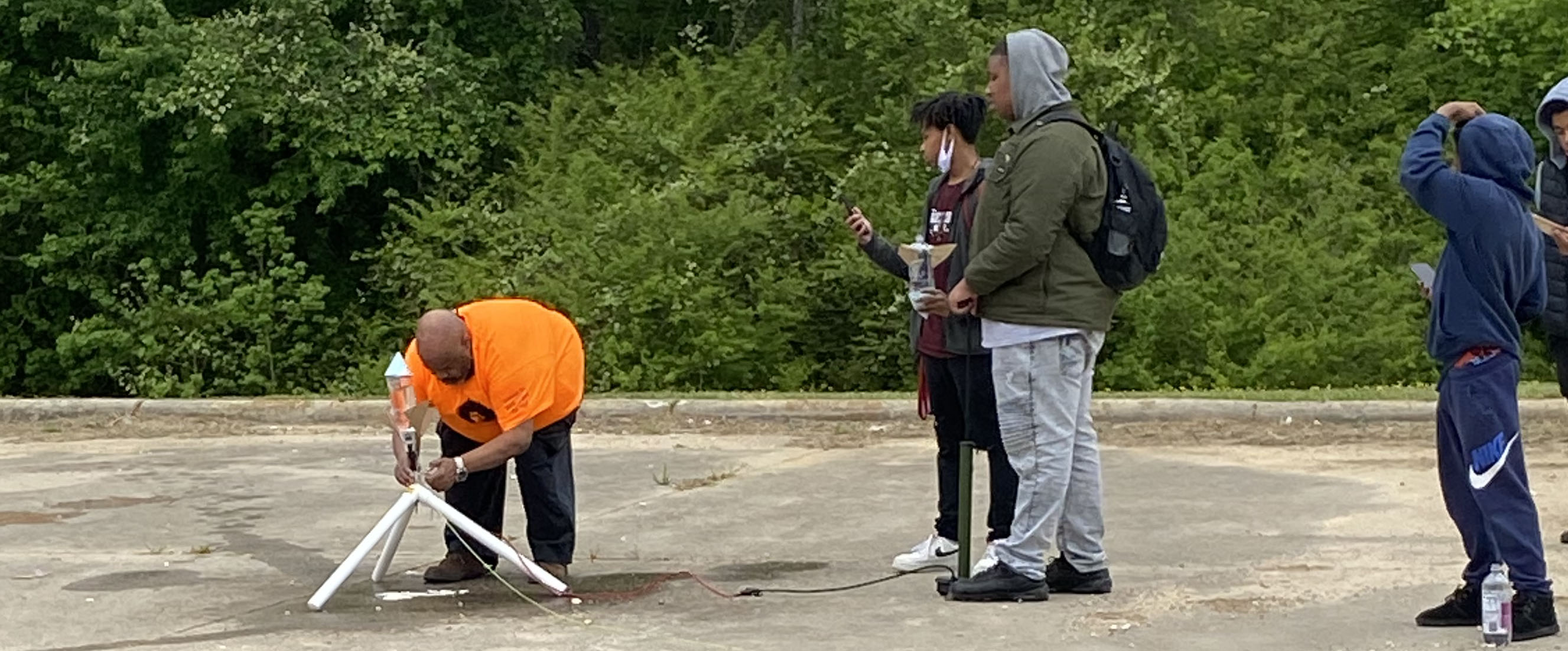 Person adjusting a homemade rocket on the ground while several students watch