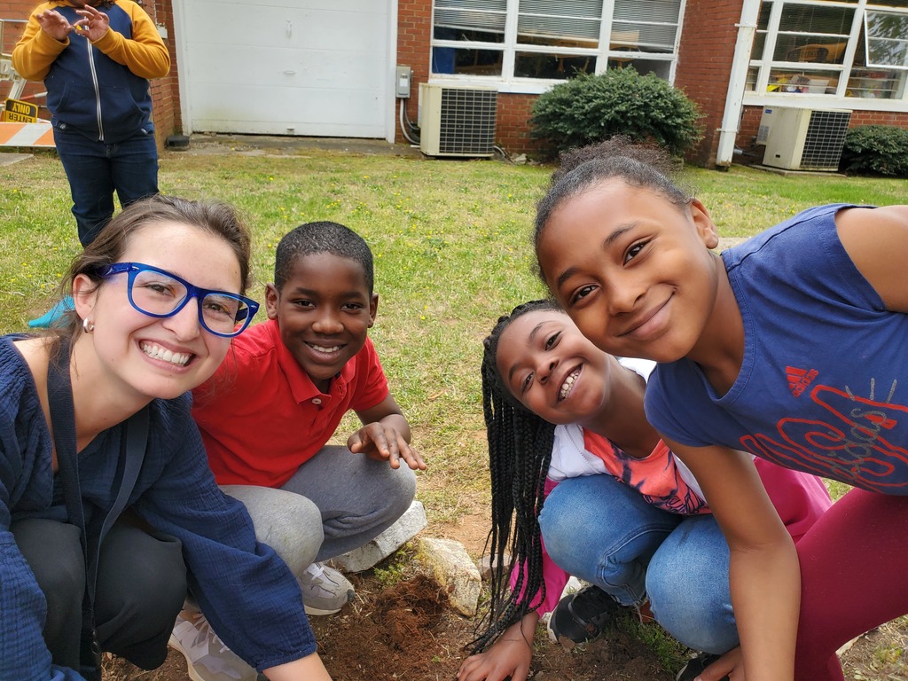A teacher and students pose for the camera while planting flowers during Earth Day. 
