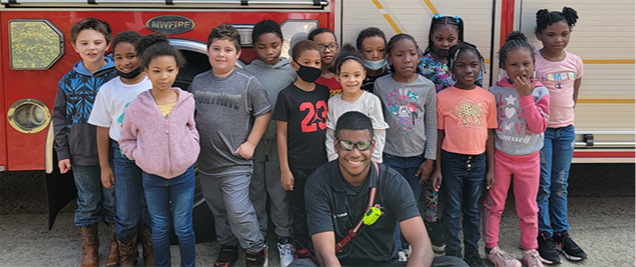 Elementary school students standing in front of a fire truck with a fire fighter