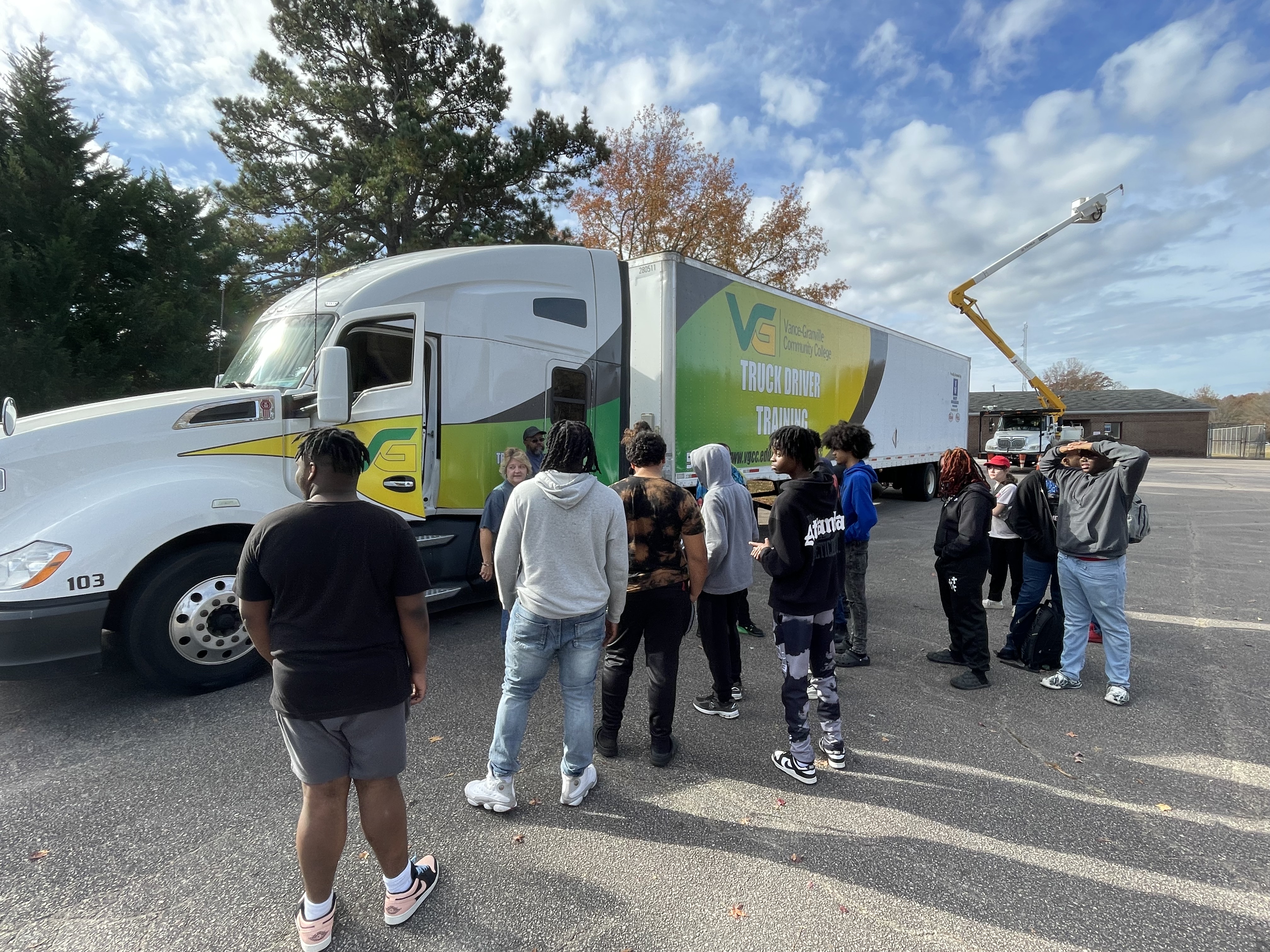 A group of students standing outside listening to an instructor talk about a VGCC 18-wheeler truck that has "VGCC Truck Driving School" on the side of it