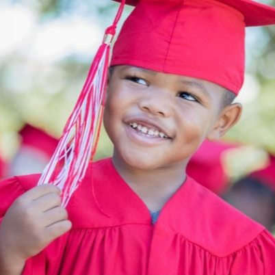 young child smiling, wearing a red graduation cap and gown