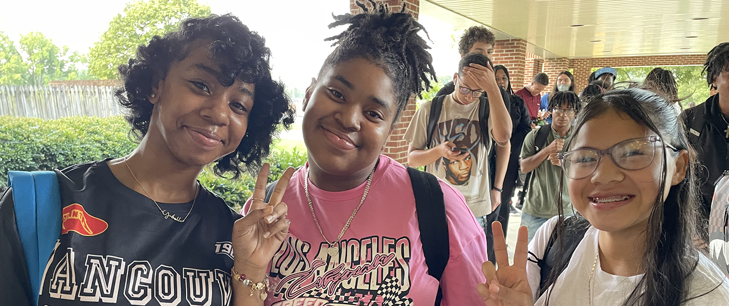 three students standing in line outside of school smiling