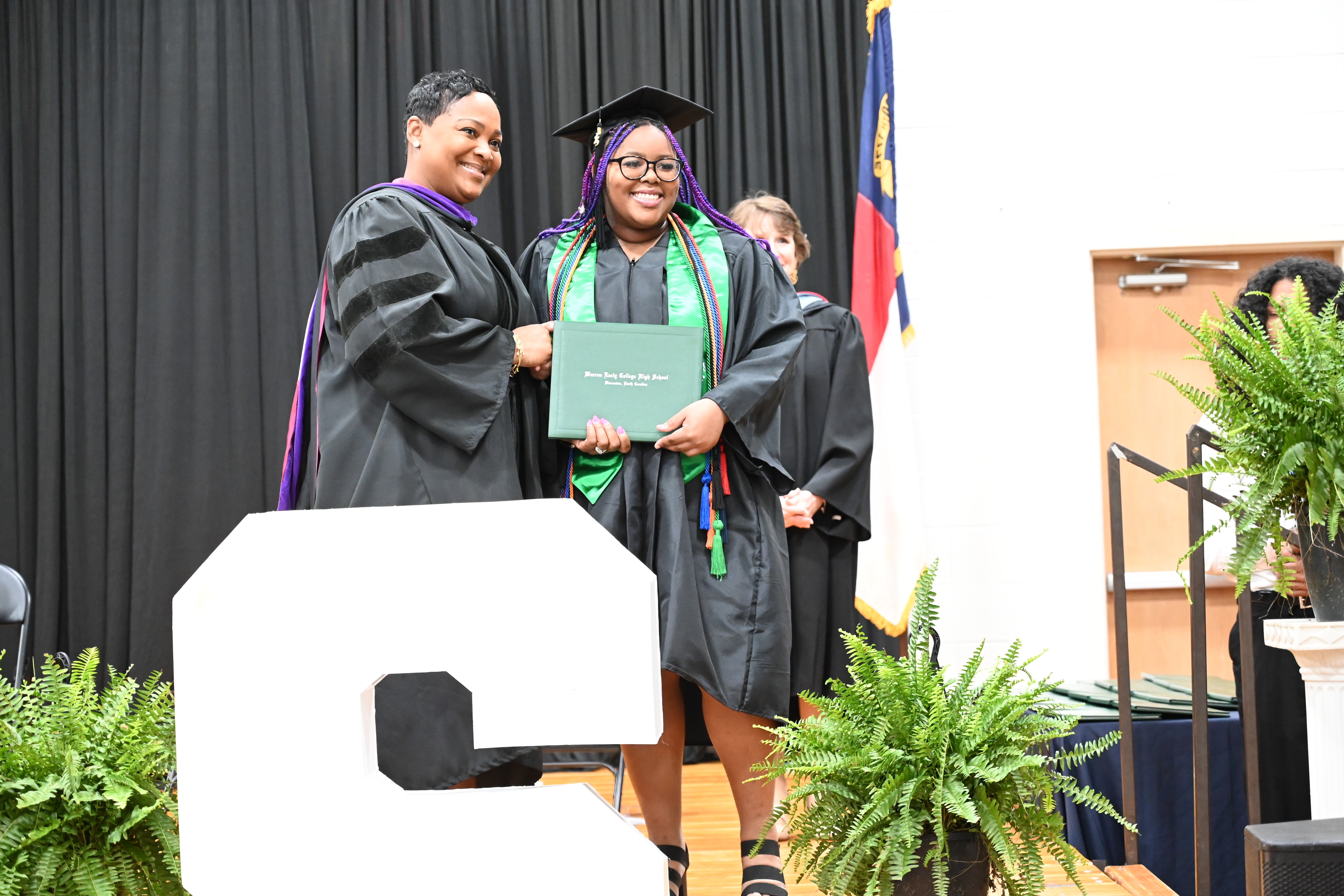 Warren Early College High School student wearing a graduation cap and gown  receiving her high school diploma and posing with the principal on the stage at graduation
