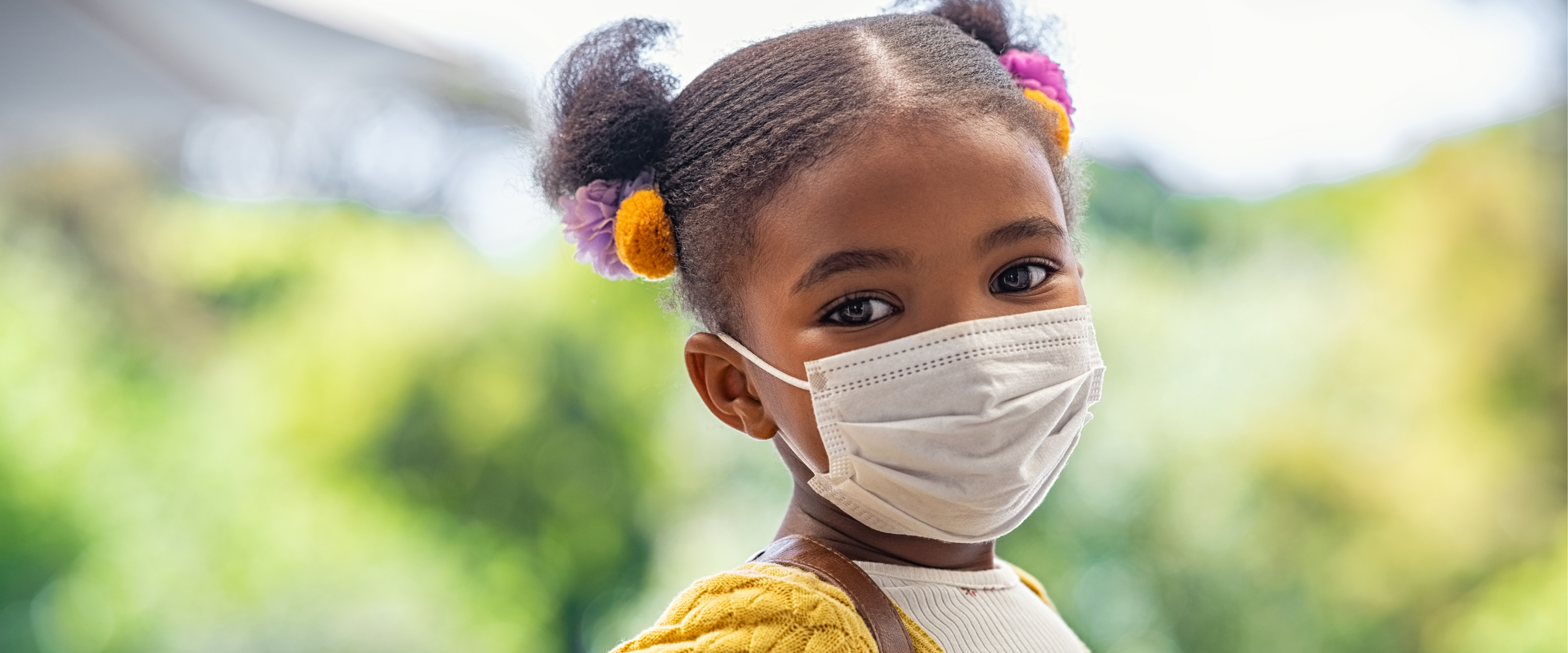 Elementary-age girl wearing face covering and smiling at the camera