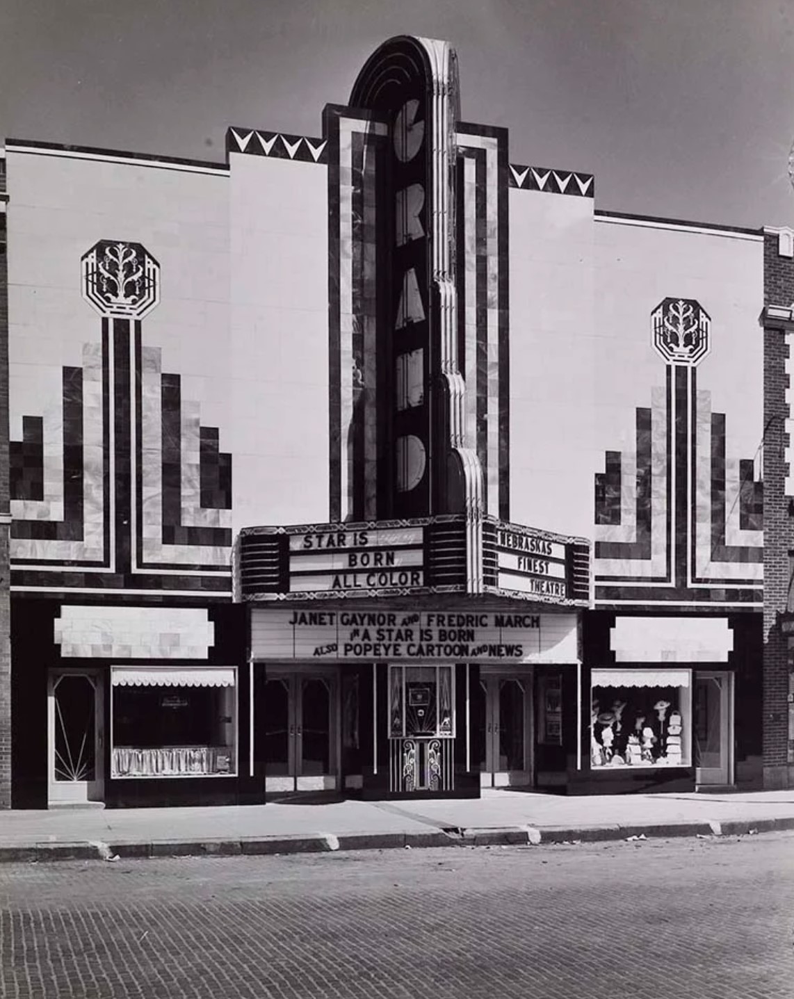  Grand Theater  318 West Third Street  In 1930, the Lyda Theater was purchased by David Kaufman and Harry Shiller. The theatre underwent extensive remodeling and was renamed "The Grand." About half the size of the present-day building, it was a modest theatre that struggled for survival in the depressed economy of a troubled town.   On May 7th, 1937, hundreds of people lined up along Third Street outside of the new theatre building. The largest neon sign in Grand Island graced the facade, which was build entirely of colored glass. It was the most beautiful modern building in town. The marquee proclaimed "Nebraska's Finest and Most Modern Theatre!" 705 people were ushered in to watch the premiere of "A Star is Born" starring Janet Gaynor, Adolph Menjou and Fredrick March.