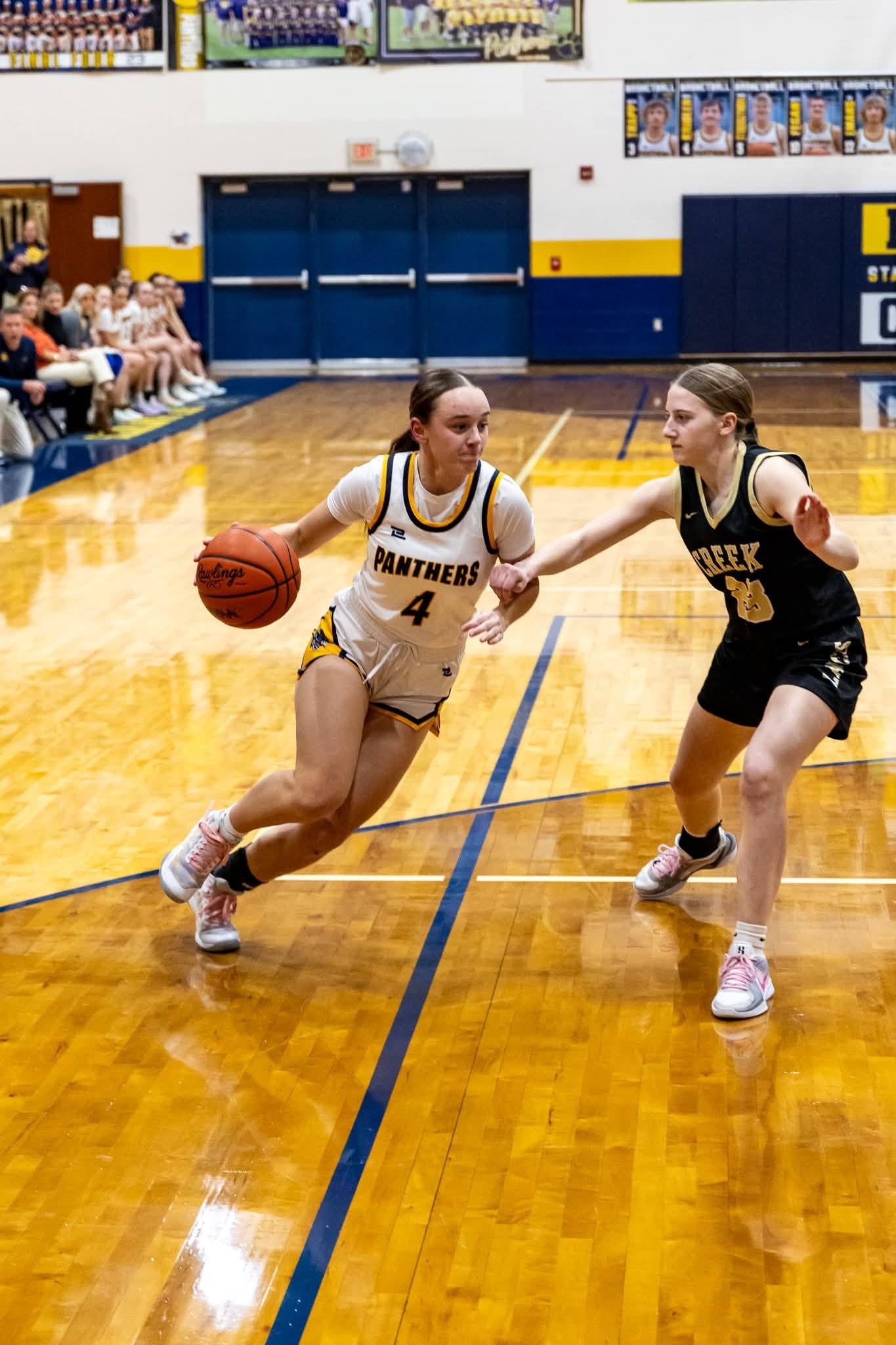 Two basketball players on a court. One wears white with Panthers 4, dribbling the ball. The other wears black with Creek 10, attempting to block.