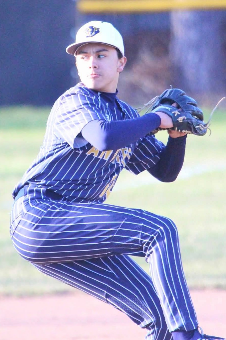 A player in a baseball uniform winds up to pitch on a baseball field with green grass.