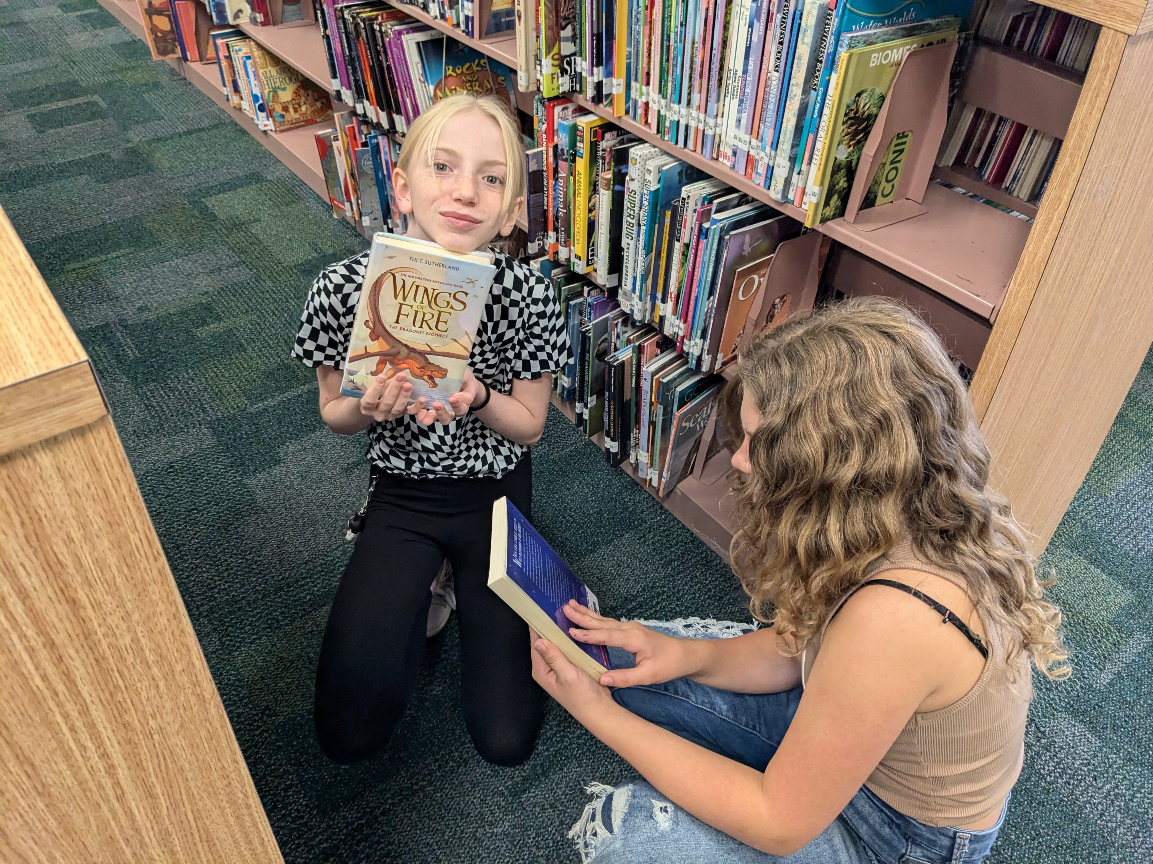 Two students looking at books on a shelf in the library