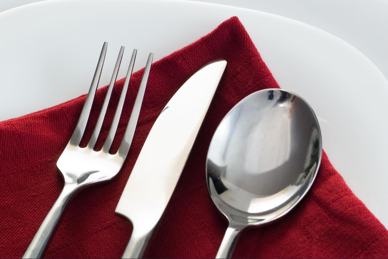 fork, knife, spoon presented on red cloth napkin on plates