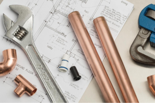 Tools and copper pipes on a blueprint. Includes wrench, pipe cutter, and pipe wrench. Background shows blue and white.