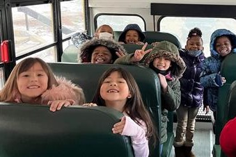 Photo showing a group of smiling students in winter gear riding a bus.