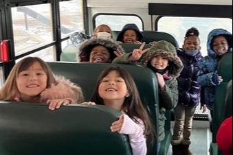 Photo showing a group of smiling students in winter gear riding a bus.