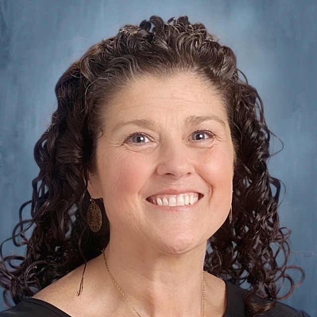 A woman with curly dark hair smiling in a professional headshot against a blue background.