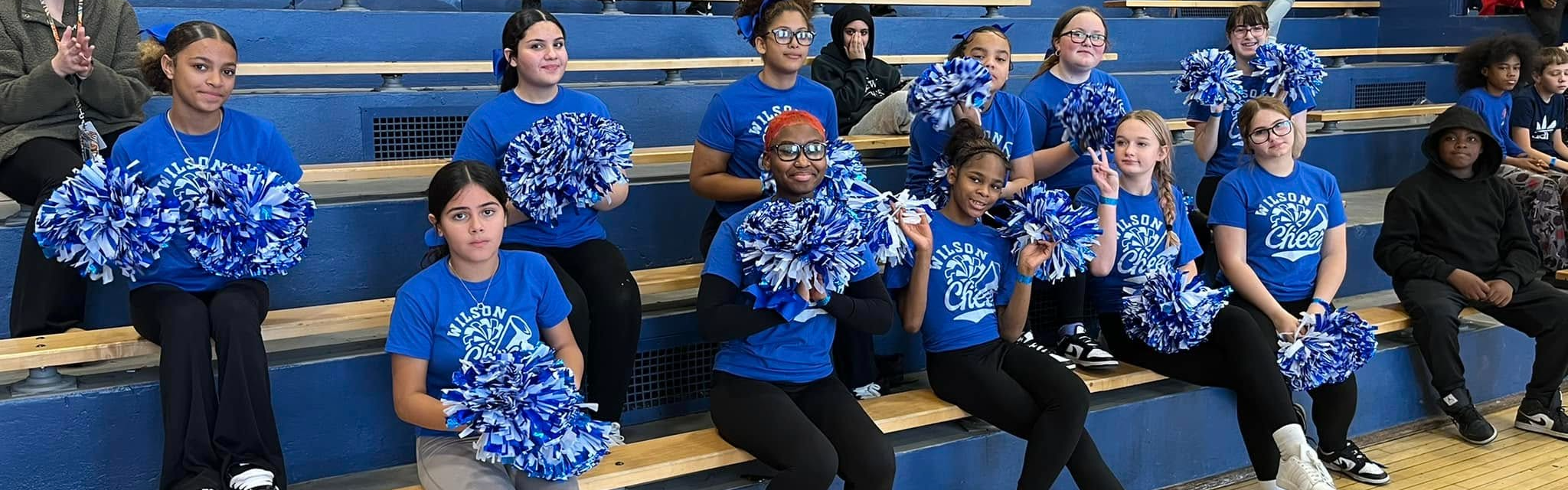 Group of students sitting in bleachers and holding pom poms.