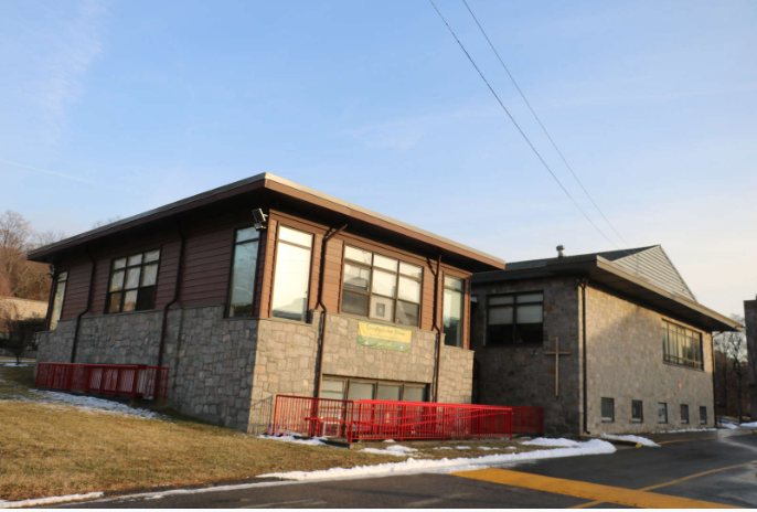 A two-story building with gray stone walls, red railings, and windows. Snow on the ground. Clear blue sky.