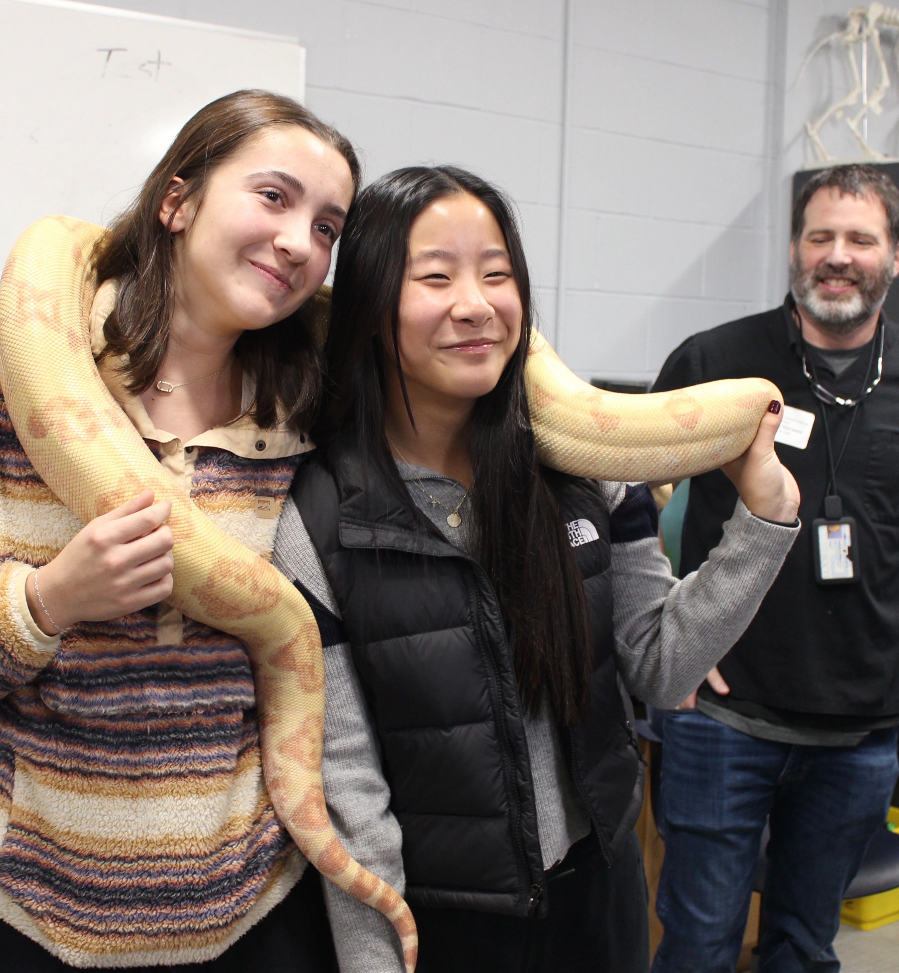two women holding a large snake as veterinary teacher looks on