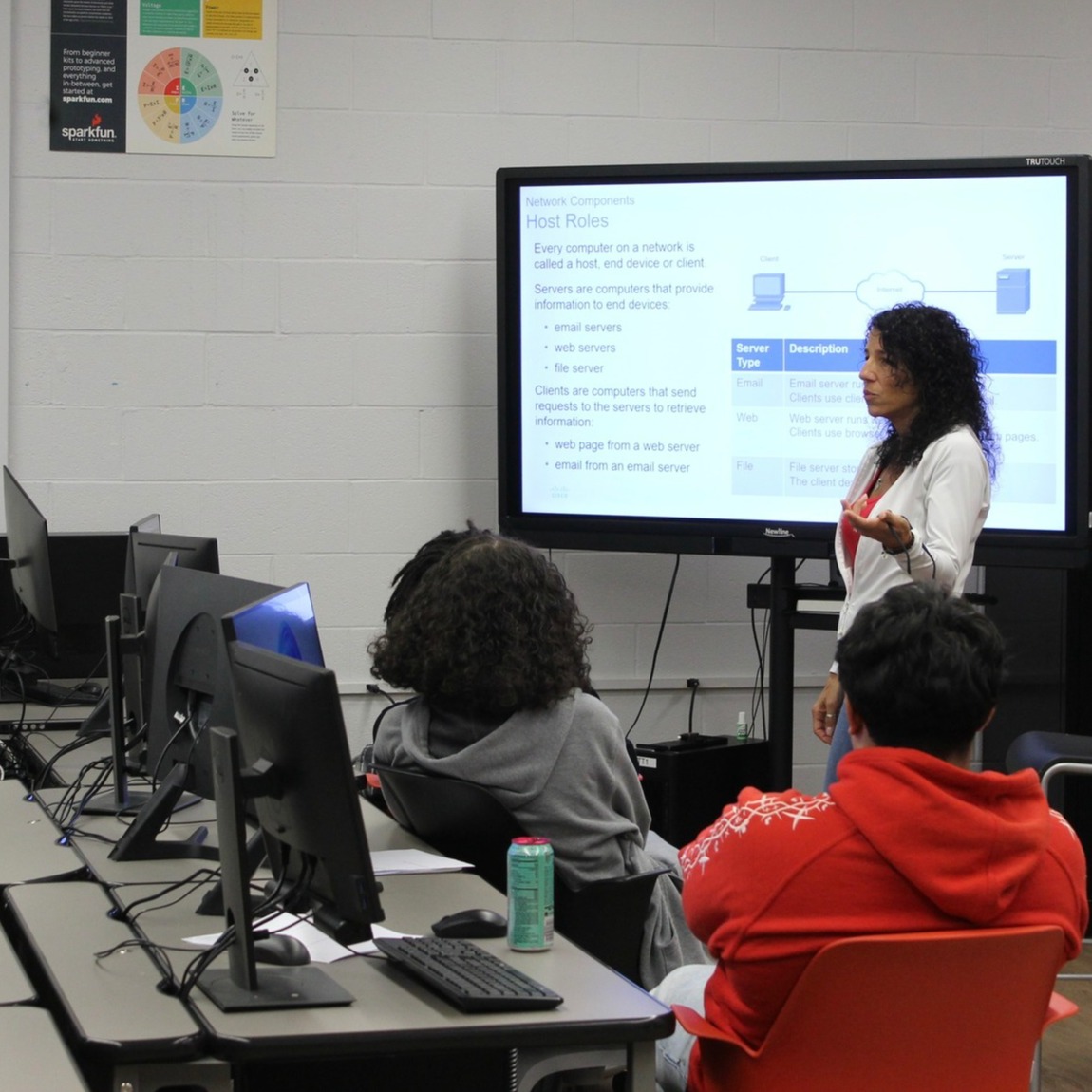 teacher stands at screen and lectures to students at workstations