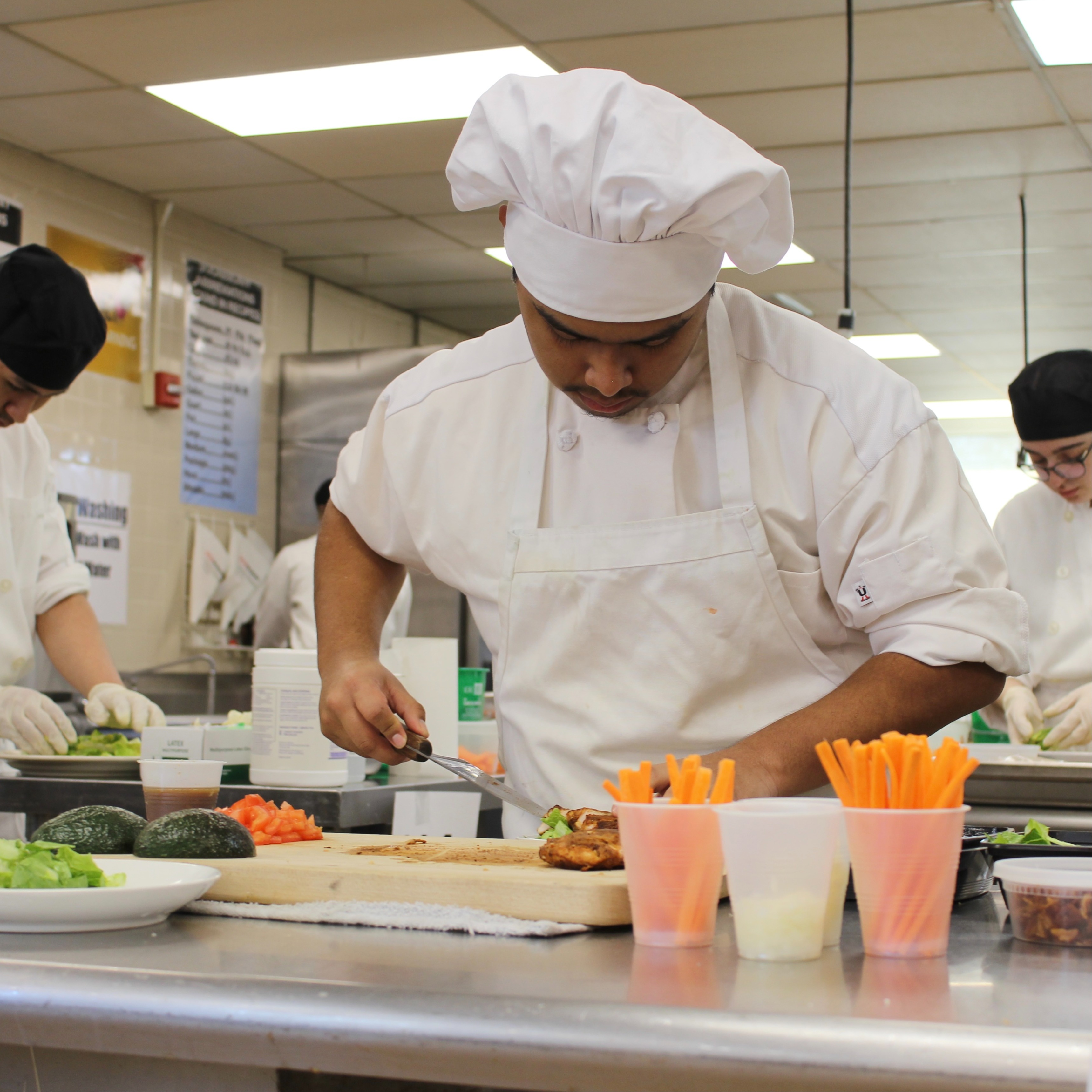 culinary arts students practice food preparation in kitchen