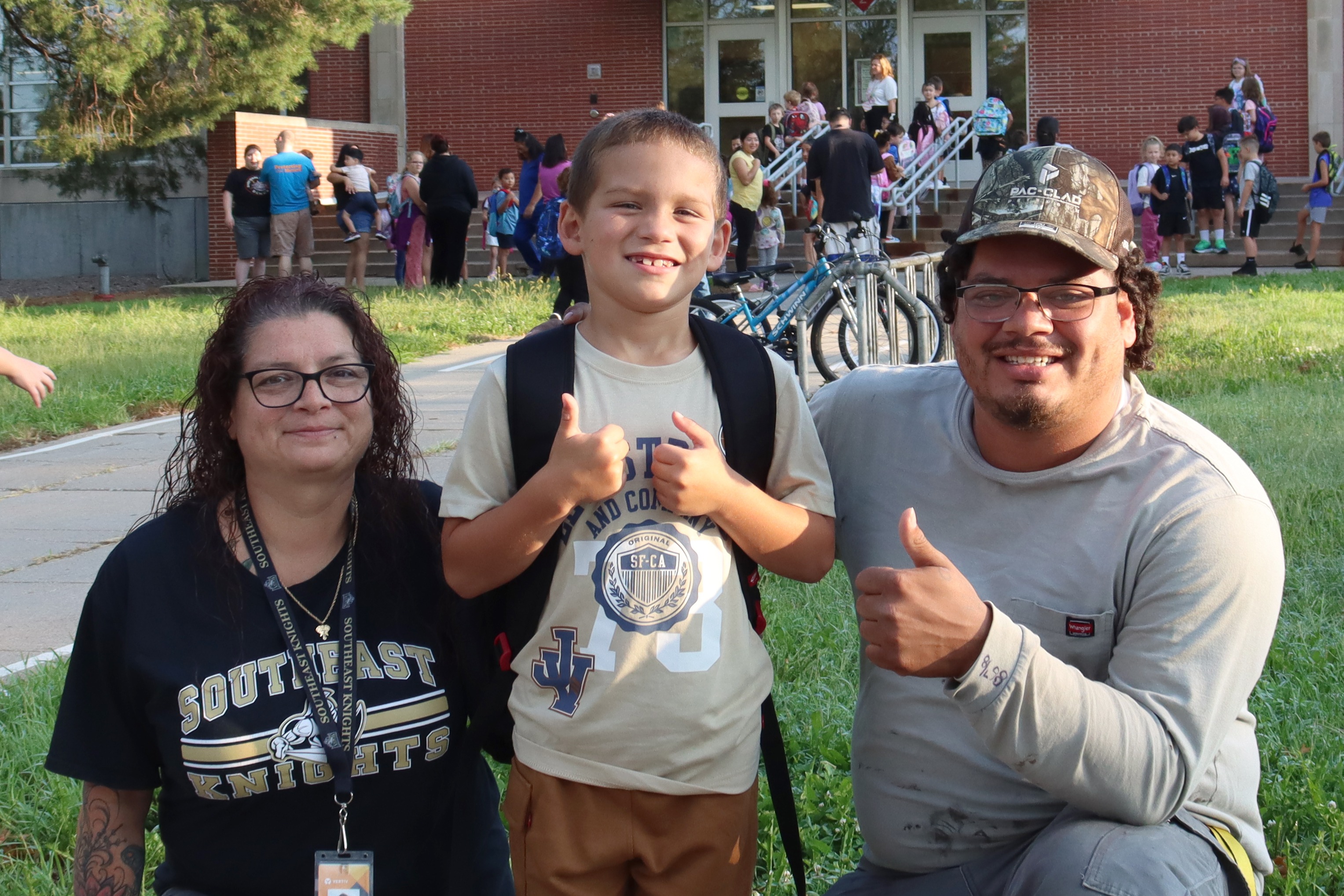Pershing family outside of school giving a thumbs up.