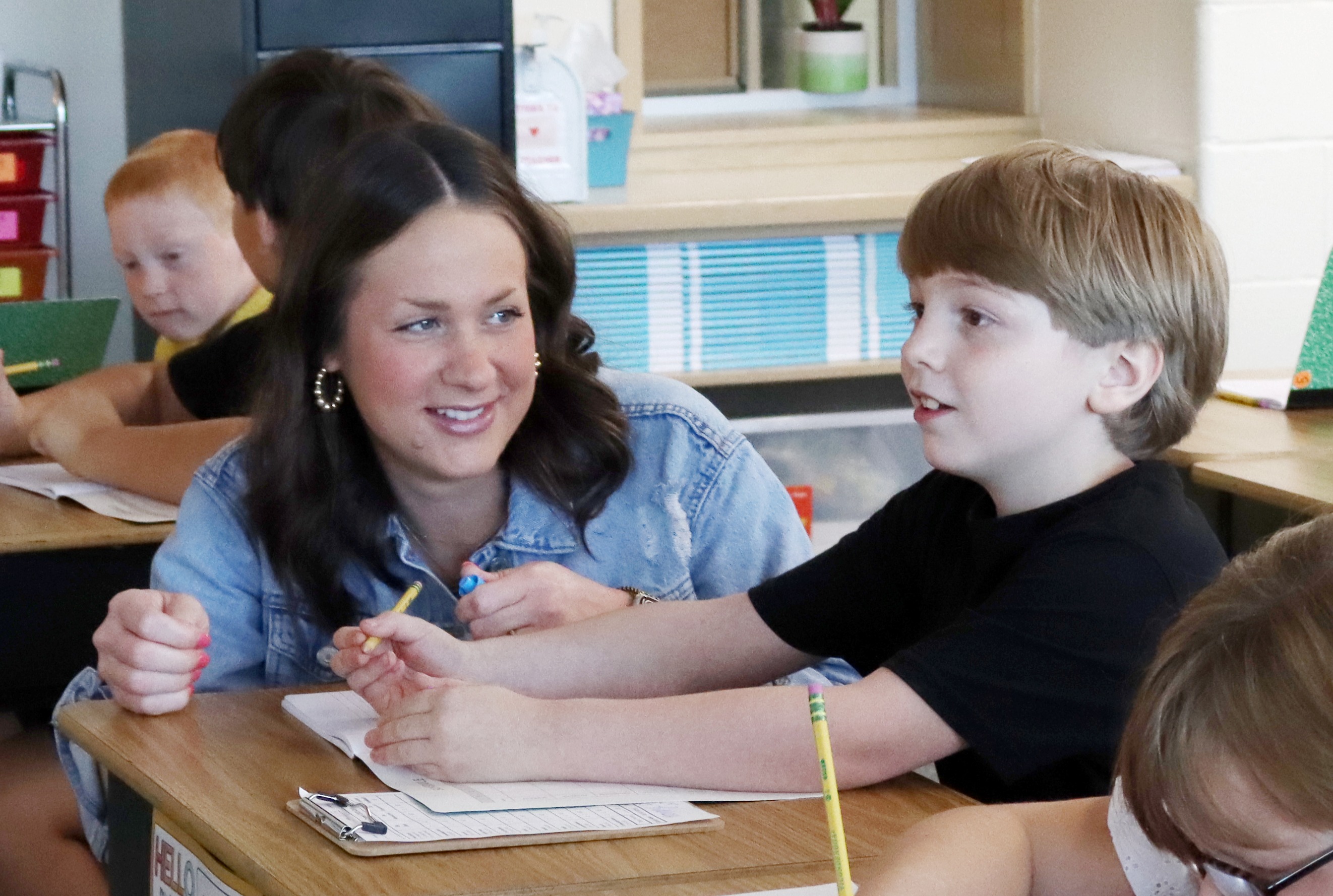 Teacher kneeling down and helping a student with math problem.